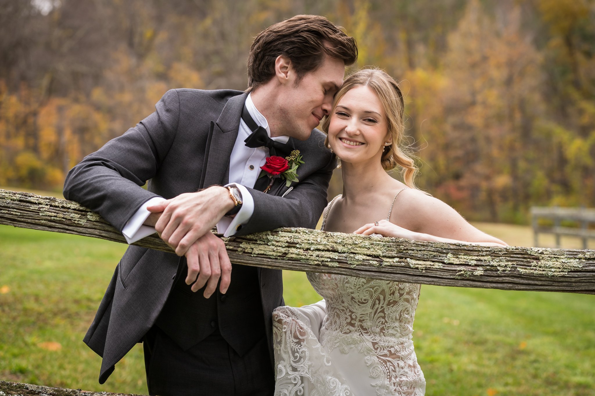 Bride and groom sharing a quiet moment leaning against a wooden fence at West Mountain Inn in Arlington, Vermont, surrounded by fall foliage