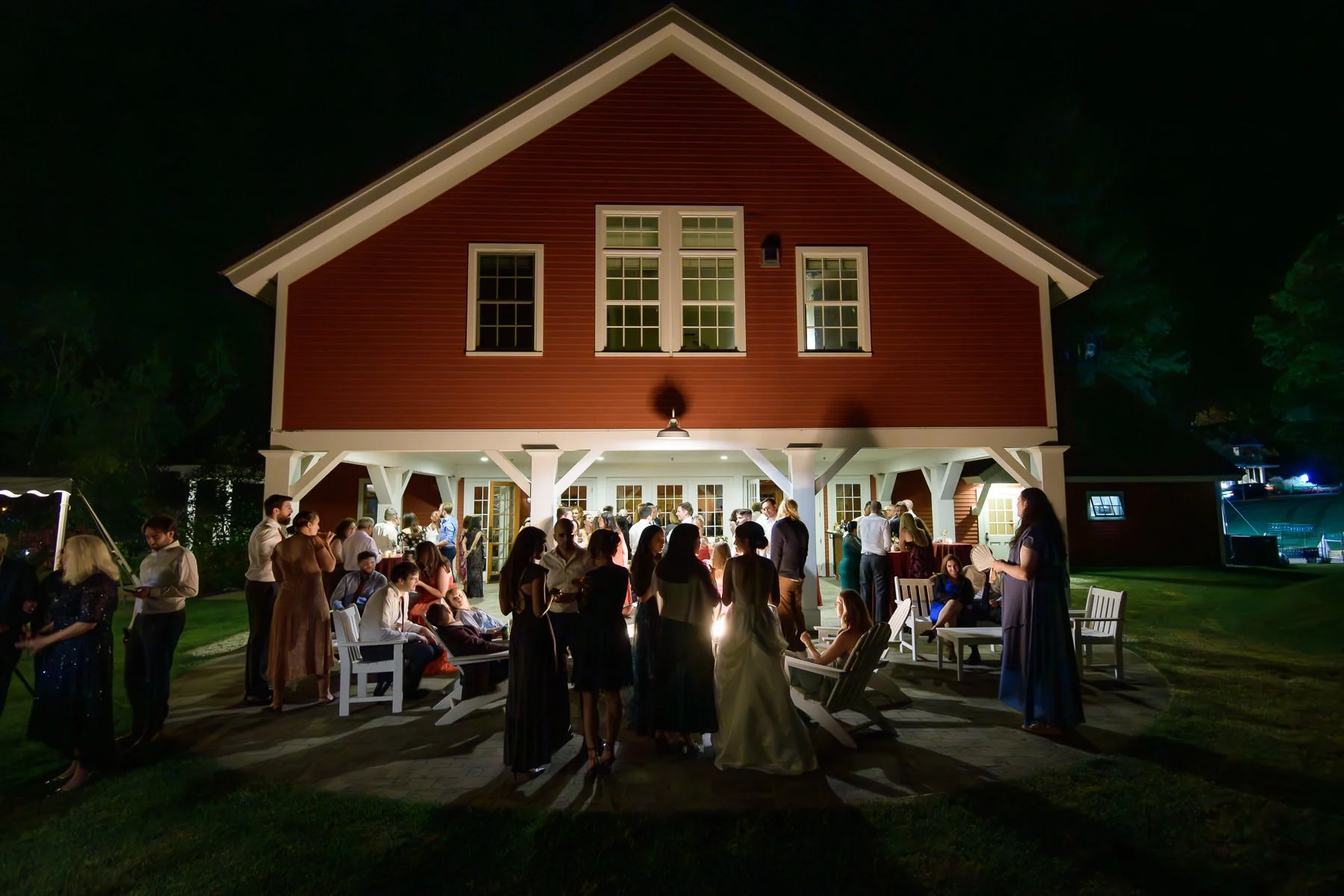 Guests gather outside the red barn at the Inn at Manchester in Vermont during the evening reception. The nighttime scene shows people mingling on the patio and lawn beneath the glow of the lit barn.