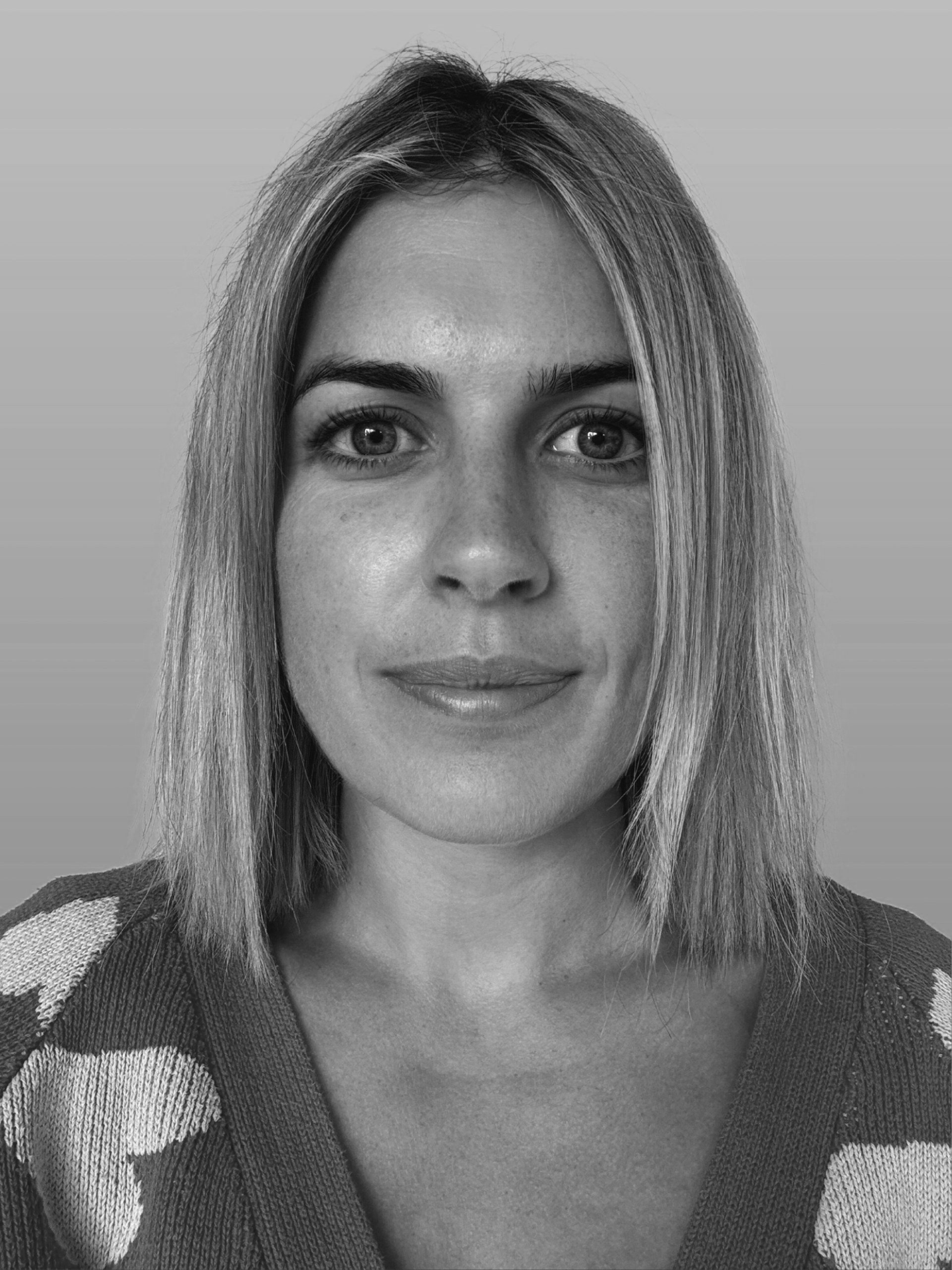 Black and white portrait of a woman with medium-length straight hair, wearing a patterned top, looking directly at the camera.