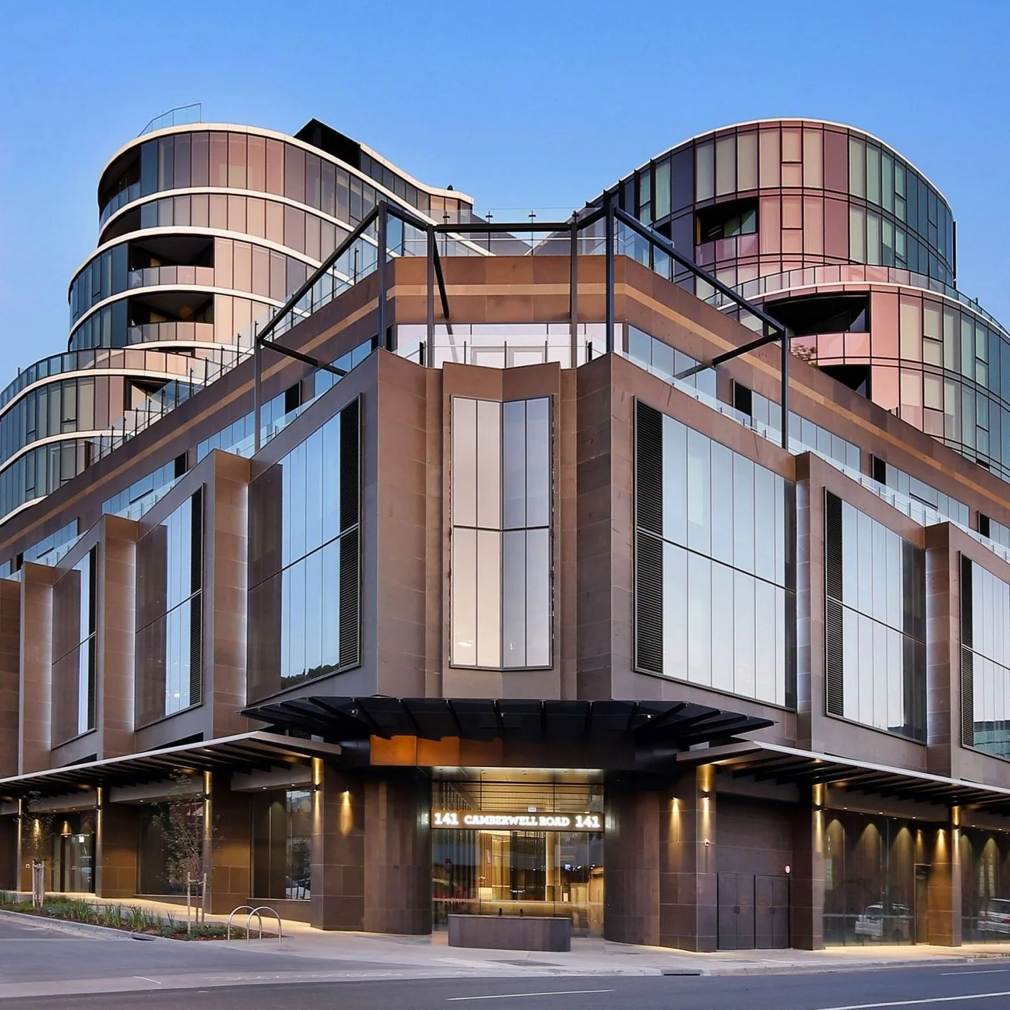 Modern multi-story building with large glass windows and rounded balconies, under a clear sky.