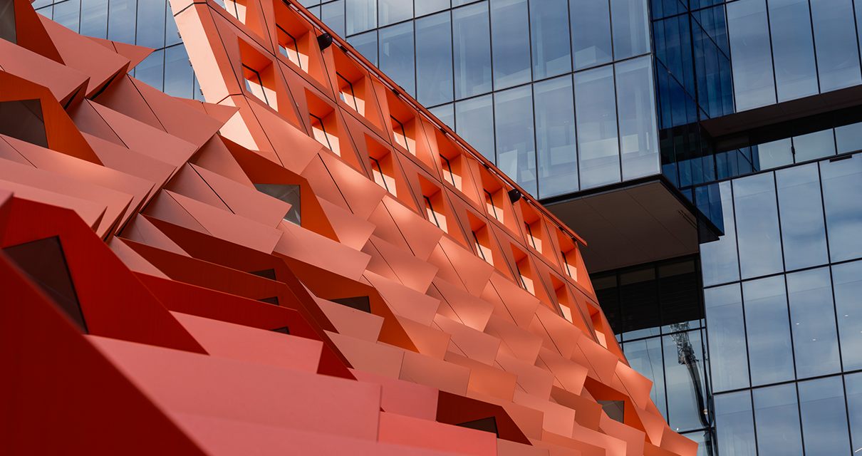Close-up view of an architectural building facade with red geometric metal panels and large glass windows.