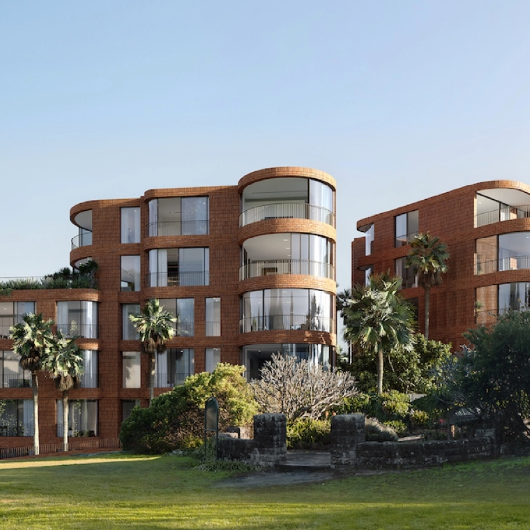 Modern red brick apartment buildings with curved glass balconies, surrounded by palm trees and greenery, under a clear blue sky.