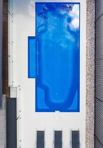 An outdoor swimming pool surrounded by a white wall and gray gravel, with three black lounge chairs against the wall. The image is upside down.