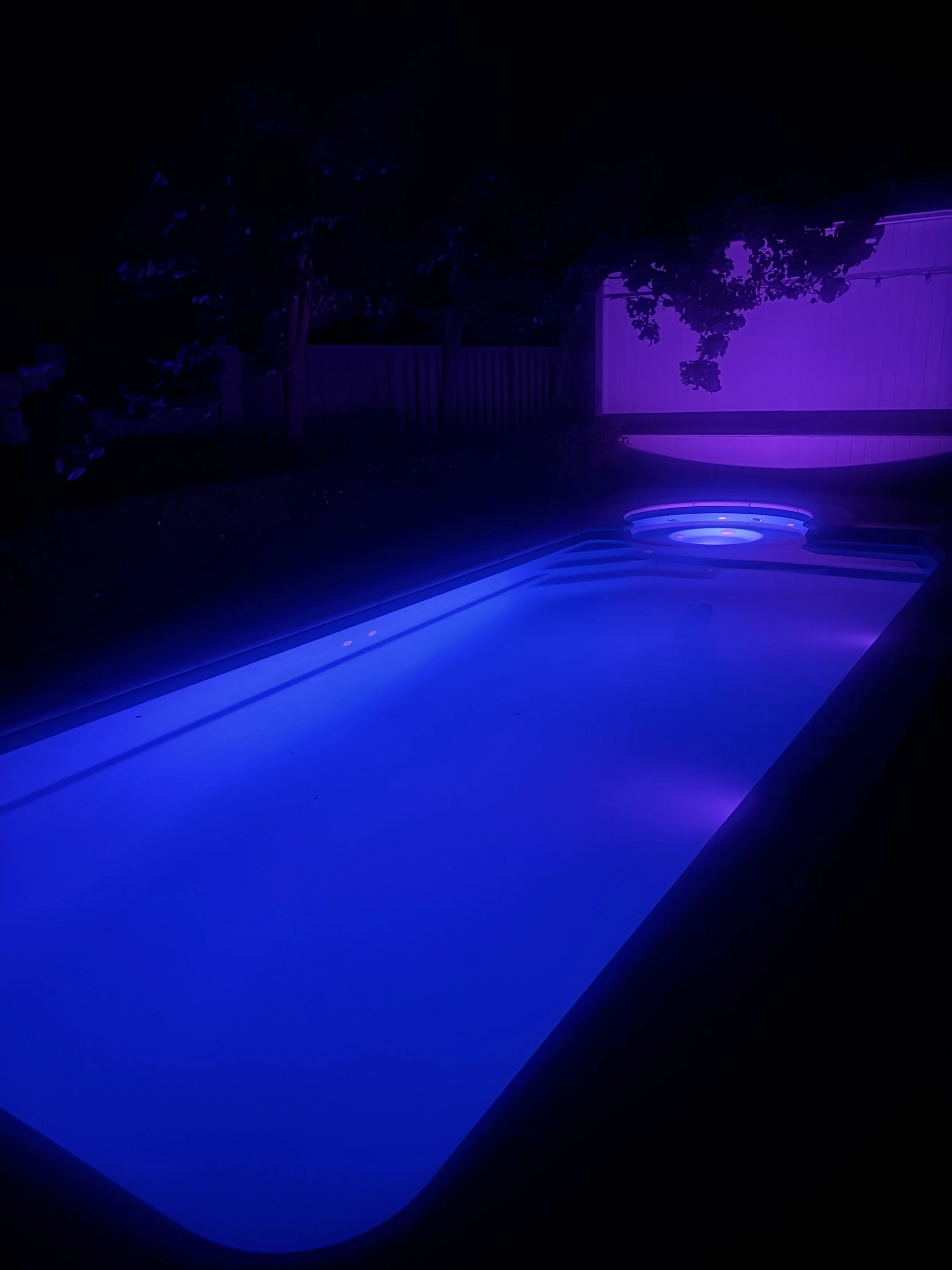 A swimming pool illuminated with blue and purple LED lights at night.