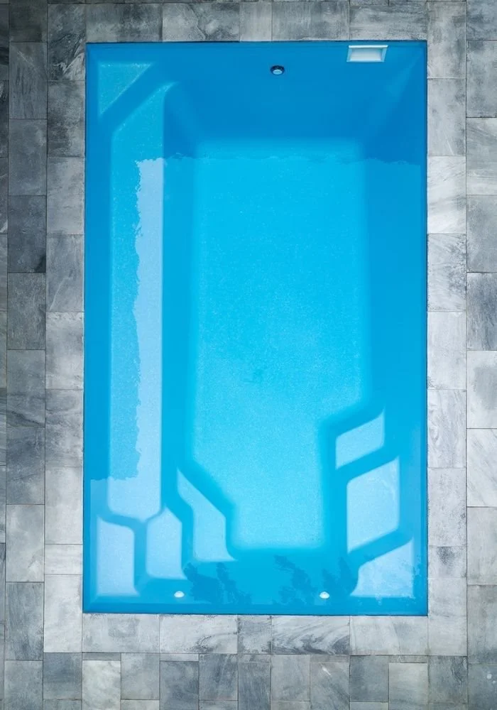 An empty indoor swimming pool with blue water, surrounded by gray stone tiles.