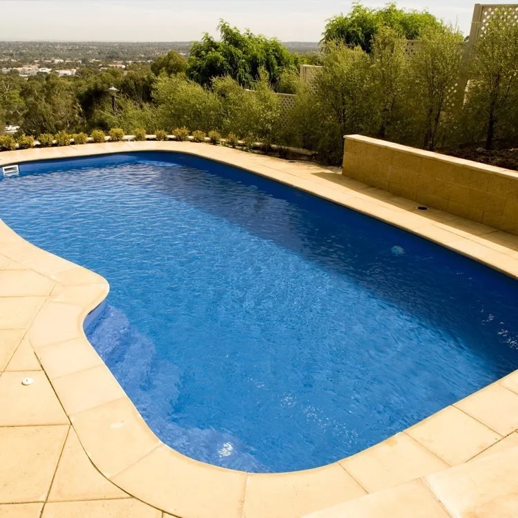An outdoor swimming pool with blue water, surrounded by a stone deck, with trees and a view of the landscape in the background.