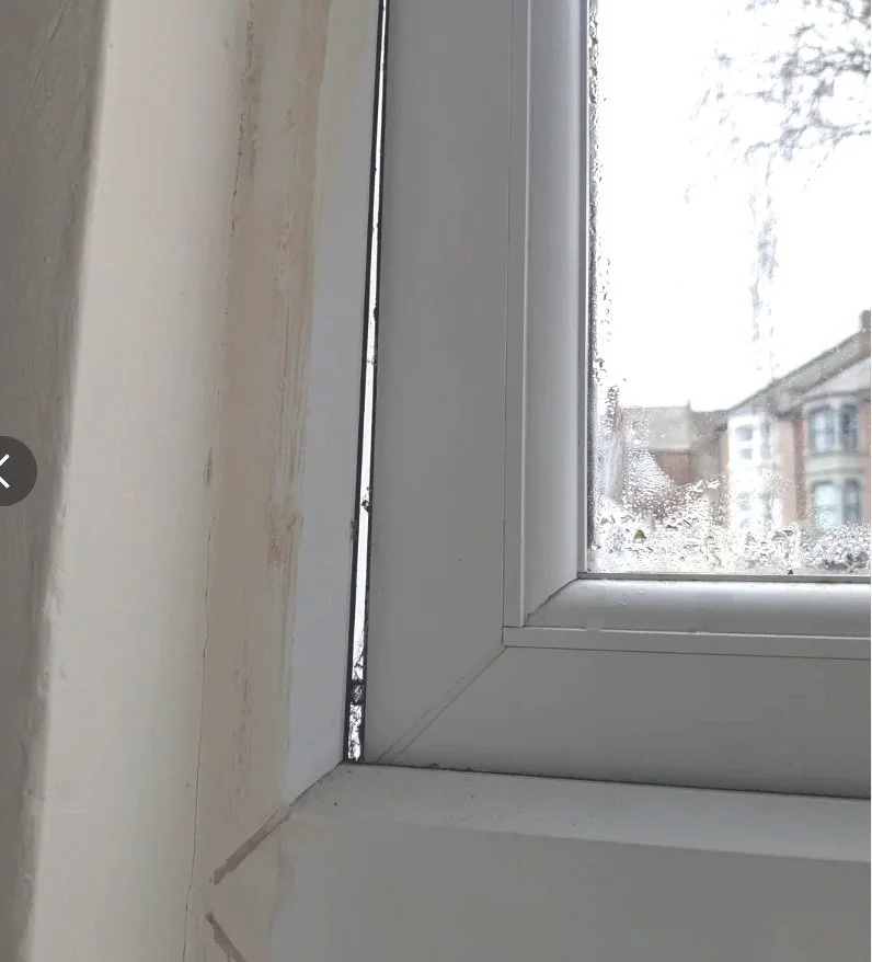 Close-up of a village window with rain on the glass, showing the outdoor buildings and trees.