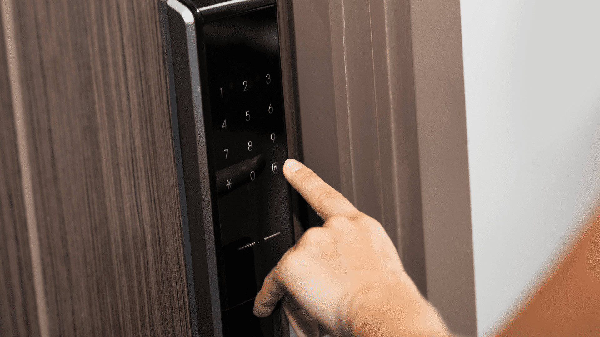 A person's hand pressing a key on a black electronic keypad lock on a door.