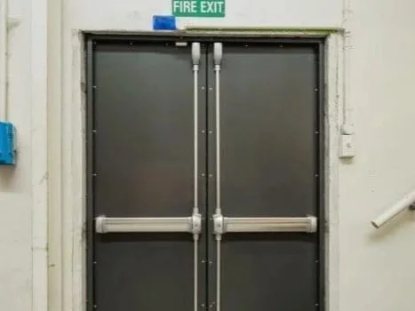 Double metal fire exit doors with a green 'Fire Exit' sign above.