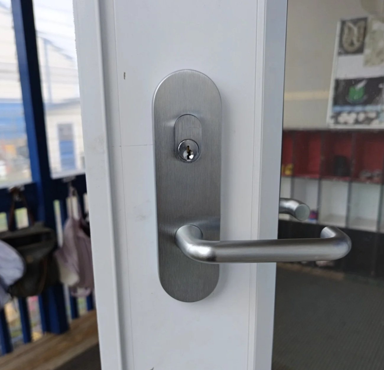 Close-up of a silver door handle and lock on a white door, with a view of the outside through a window on the left.