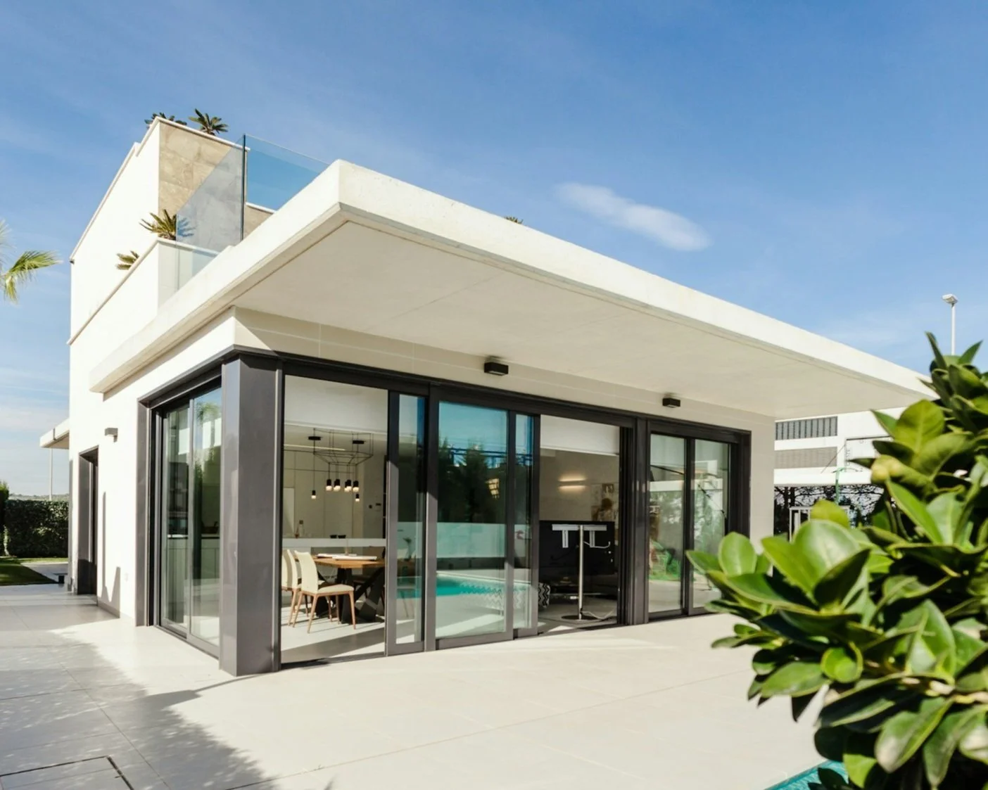Modern two-story house with large glass doors, patio, and balcony, under a clear sky.