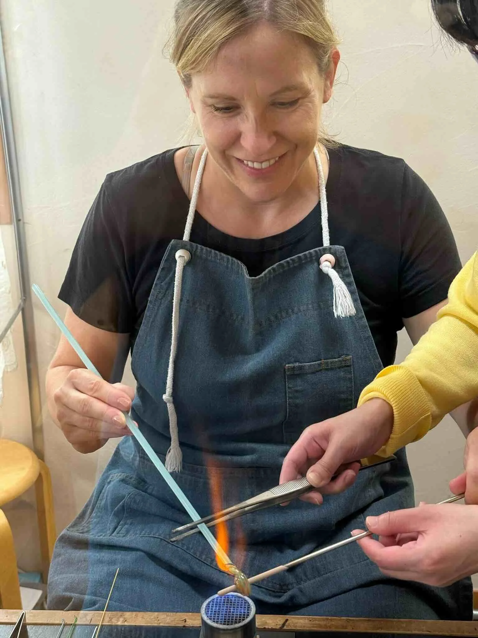 Adult making a tonbodama glass bead over a flame with hands-on guidance from instructors at a glass studio in Hakuba, Japan.