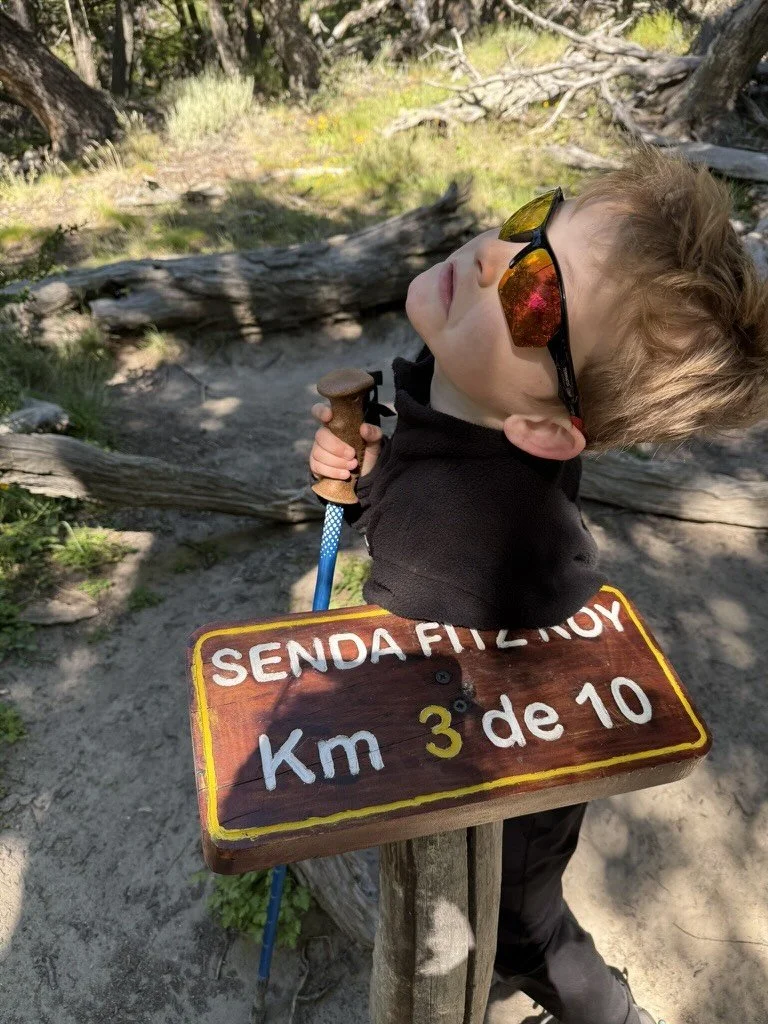 Eight-year-old hiker jokingly posing as exhausted beside the 3-kilometer marker on the Fitz Roy trail in Patagonia, Argentina.