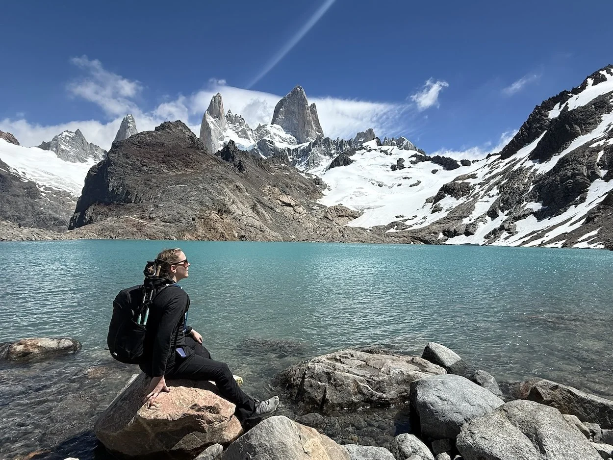 Woman sitting beside Laguna de los Tres with Mount Fitz Roy rising behind the lake in Los Glaciares National Park, Patagonia, Argentina.
