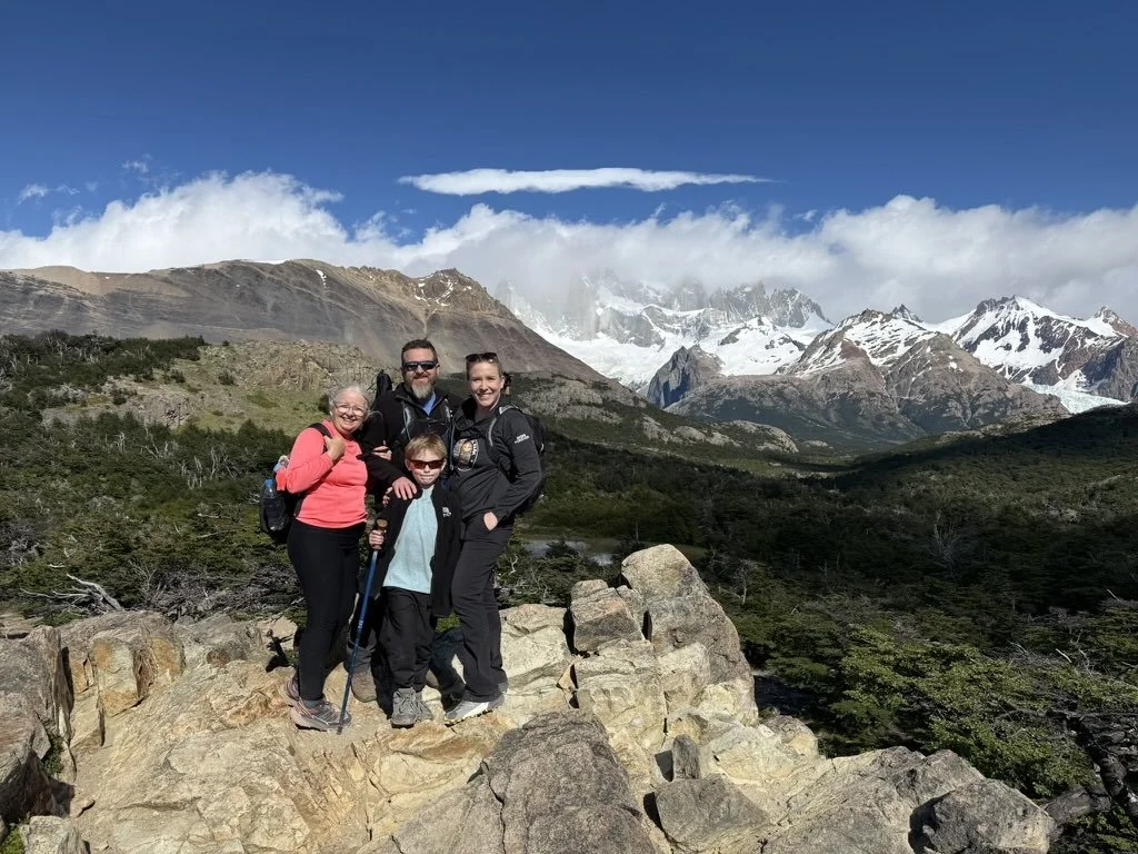 Family of four at a viewpoint on the Laguna de los Tres trail with the Fitz Roy massif and snow-covered mountains behind them