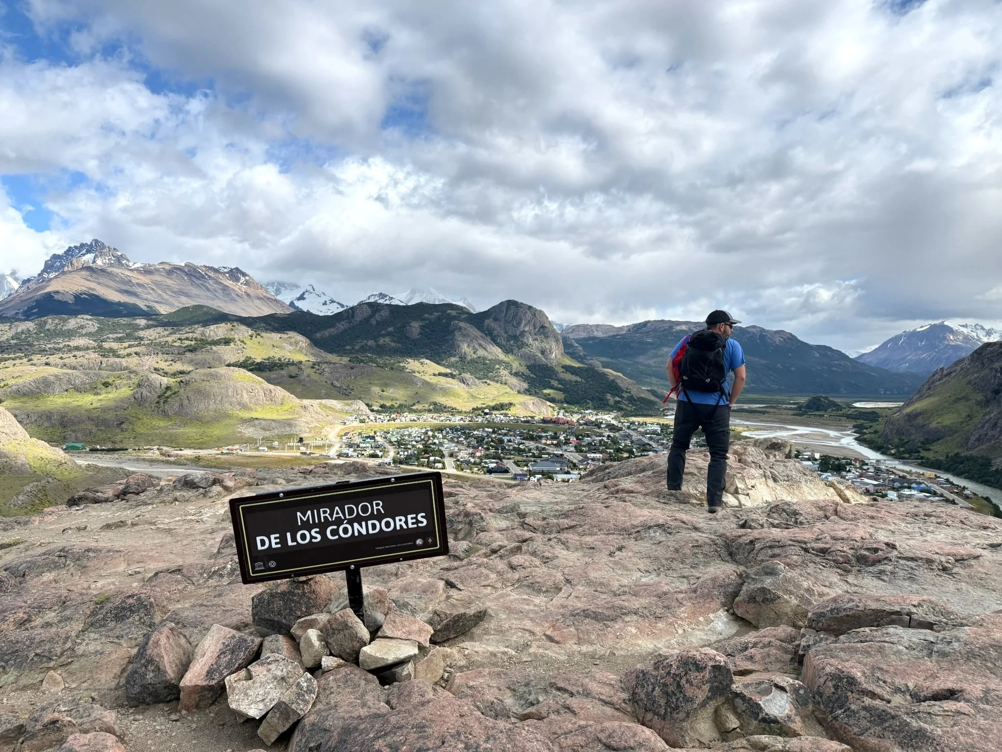 Mirador de los Cóndores lookout above El Chaltén, Patagonia, with a hiker standing near the viewpoint and the town below.
