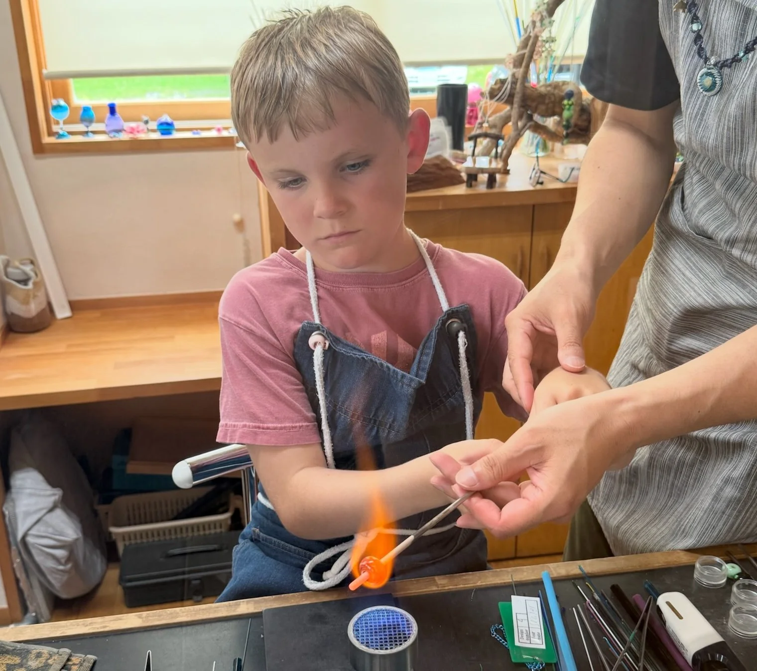 Eight-year-old child making a tonbodama glass bead over a flame with guidance from an instructor at Gaku Glass in Hakuba, Japan.