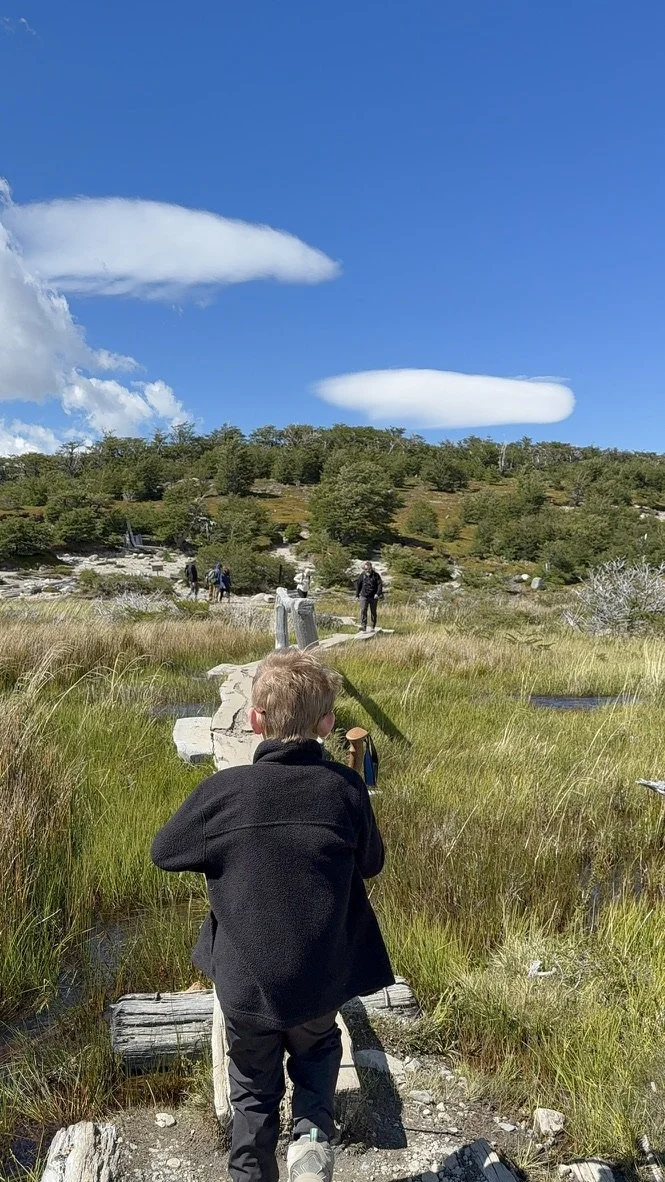 Child hiking across a wooden boardwalk through a wetland section of the Laguna de los Tres trail near El Chaltén.