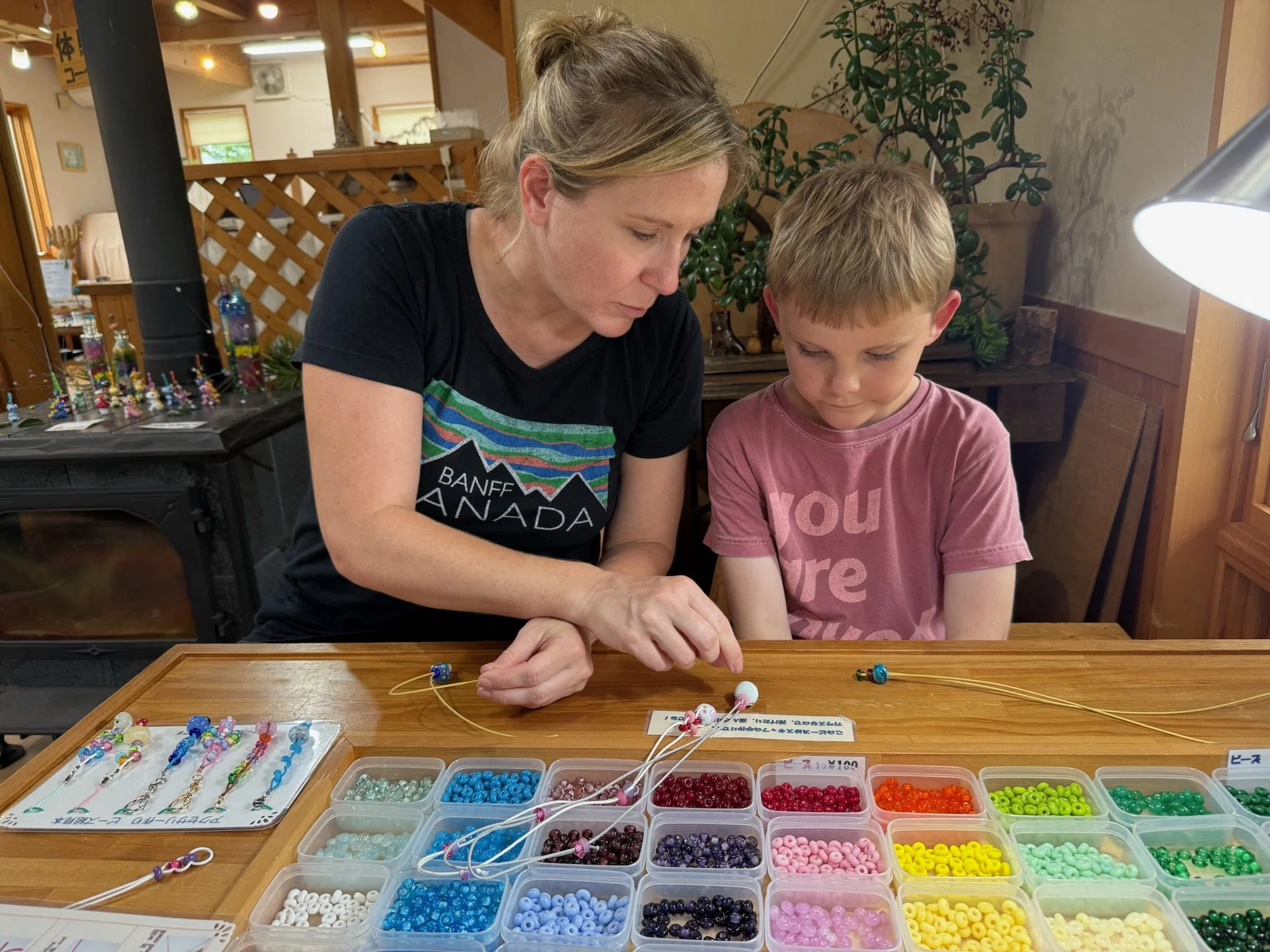 Mother and eight-year-old child choosing colorful glass beads to finish handmade tonbodama pieces at a workshop in Hakuba, Japan.