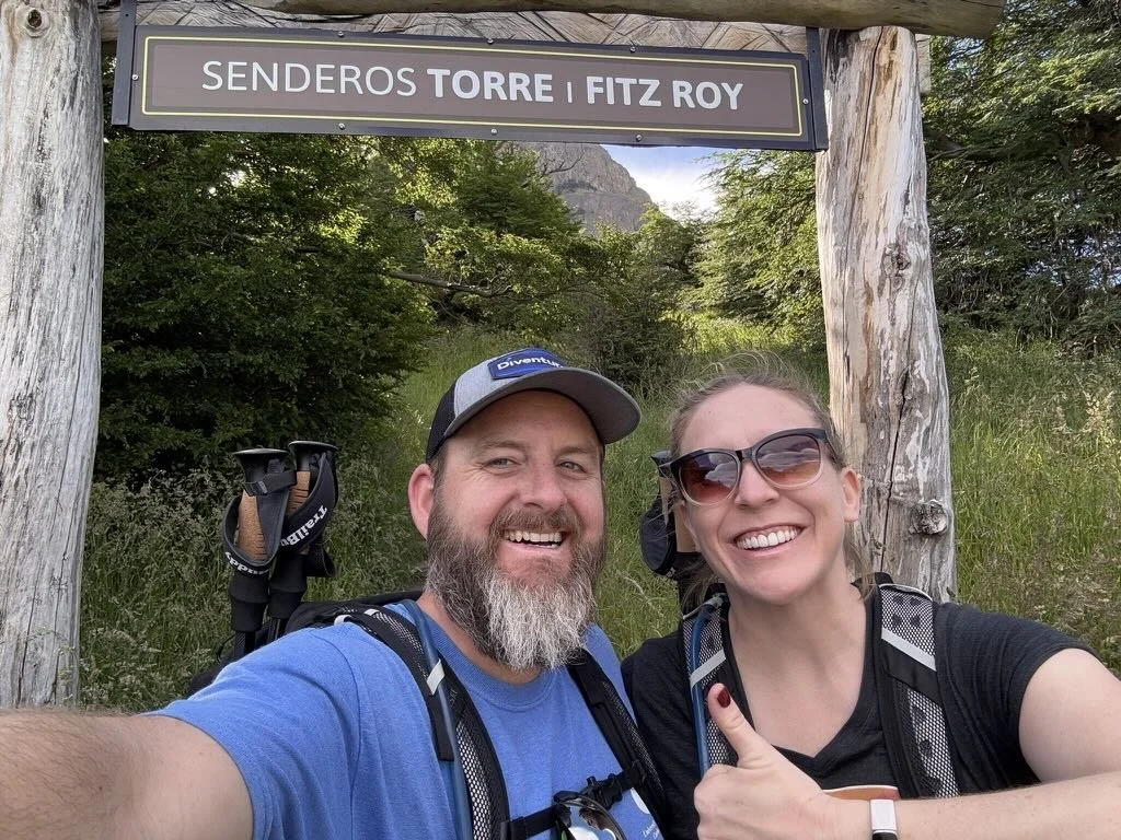 Couple smiling at the end of their hike beneath the Senderos Torre and Fitz Roy trail sign in El Chaltén, Argentina.