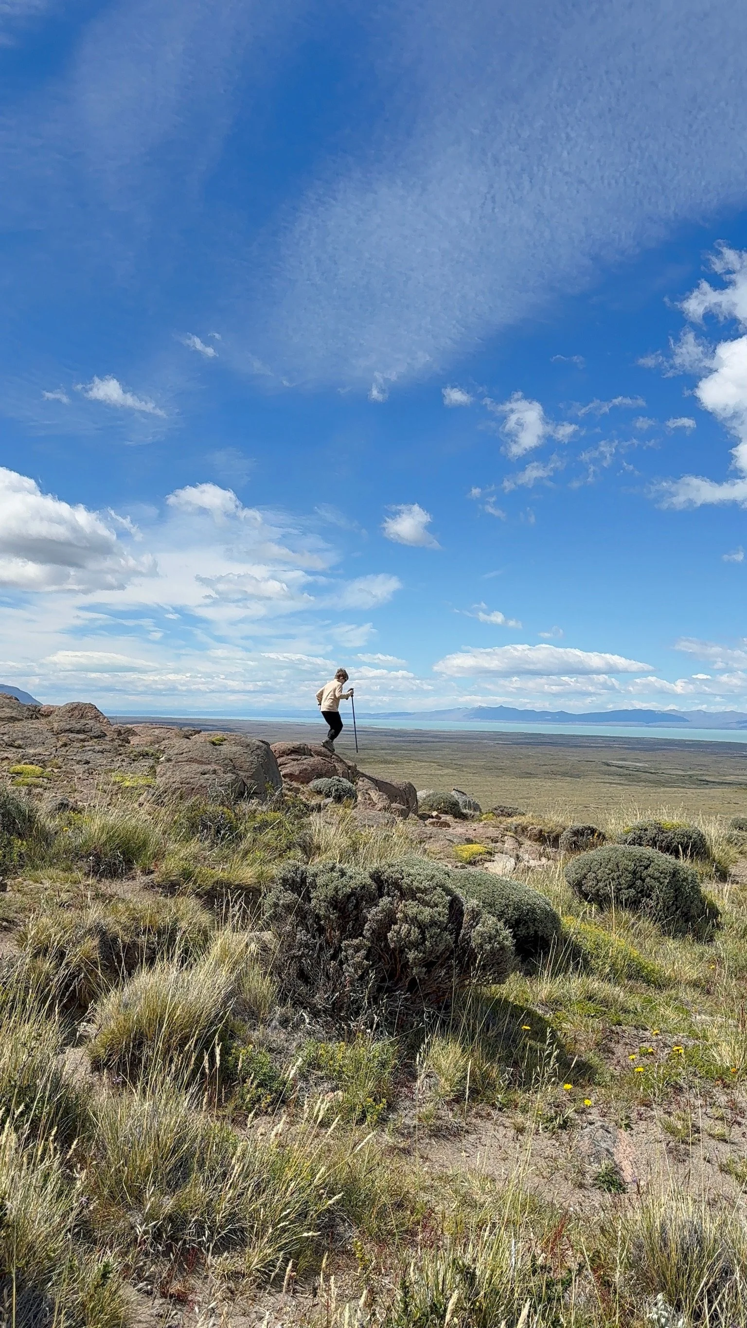 A child hiking across open, rocky terrain near El Chaltén, Patagonia, with wide views of the steppe and distant mountains.