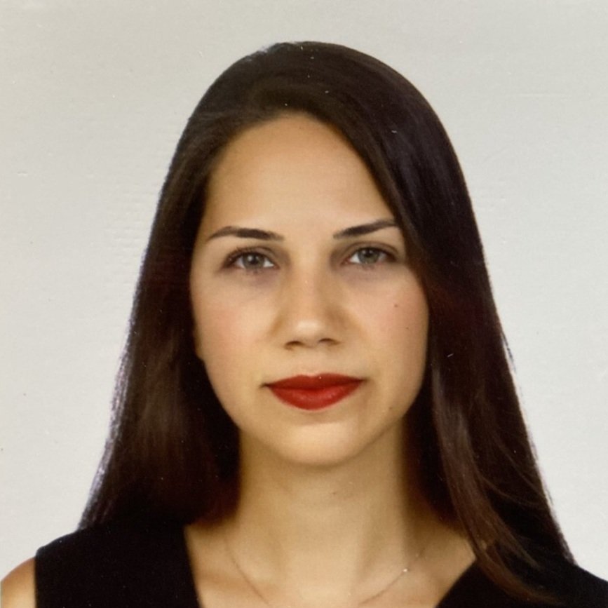 A portrait of a woman with straight dark brown hair, light skin, red lipstick, wearing a black top, and a delicate necklace against a neutral background.