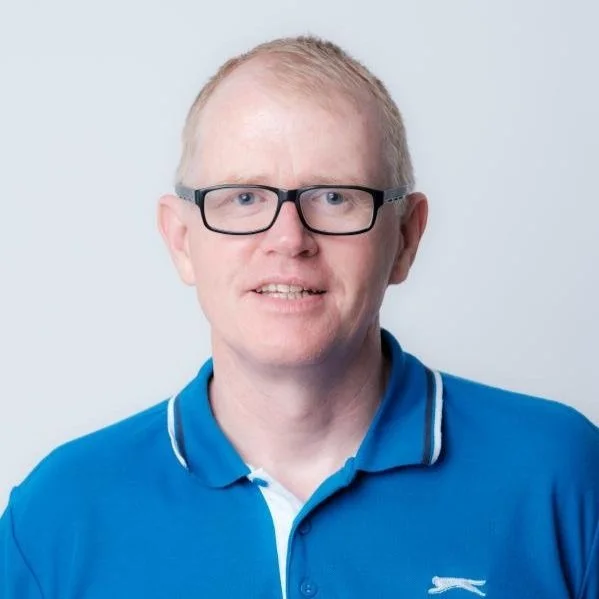 Portrait of a man with glasses wearing a blue polo shirt against a light background.