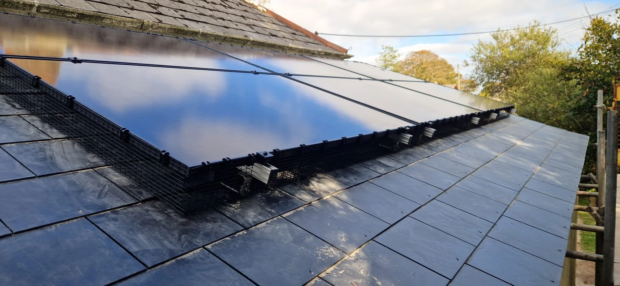 Solar panel installed on a tiled roof, reflecting the sky and clouds.