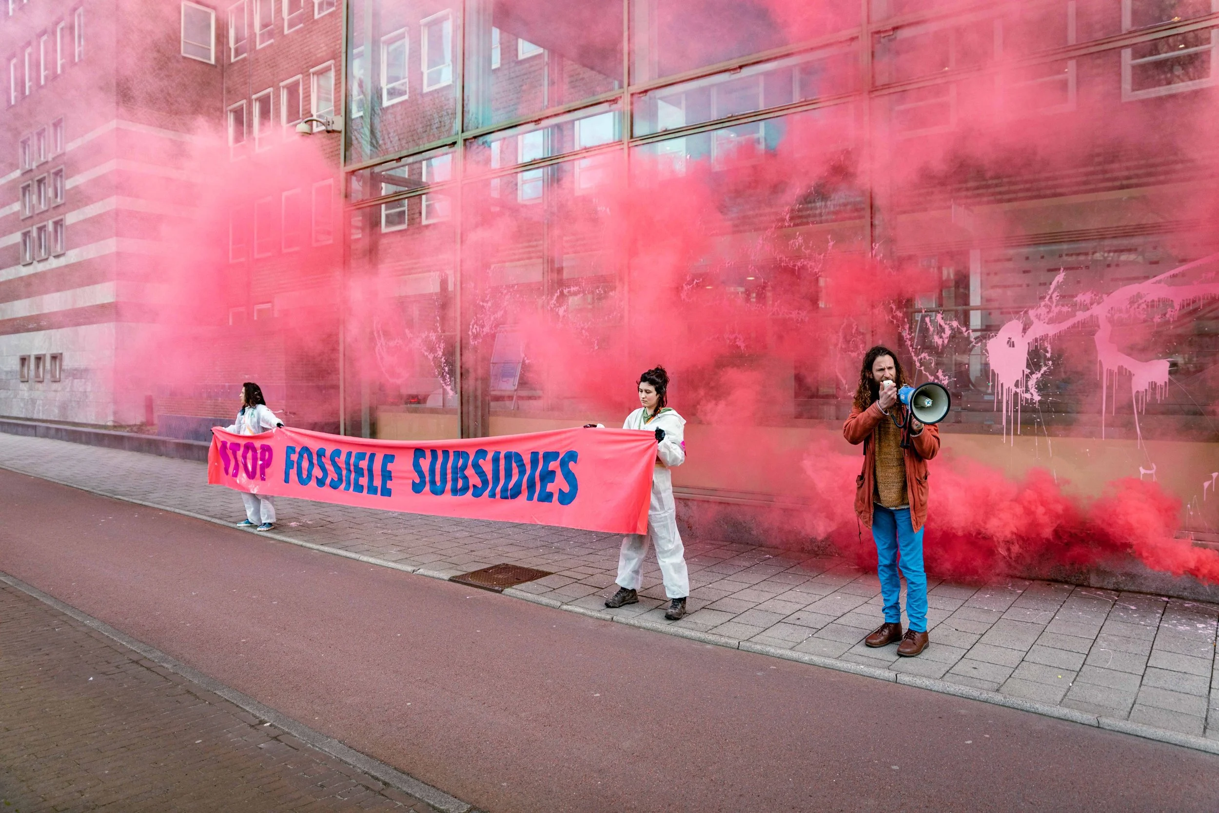Protesters holding a pink banner that reads 'STOP FOSSIL SUBSIDIES' with pink smoke in the background.