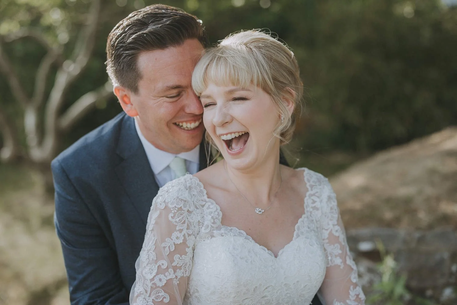 A happy couple in wedding attire sharing a joyful moment outdoors in nature.