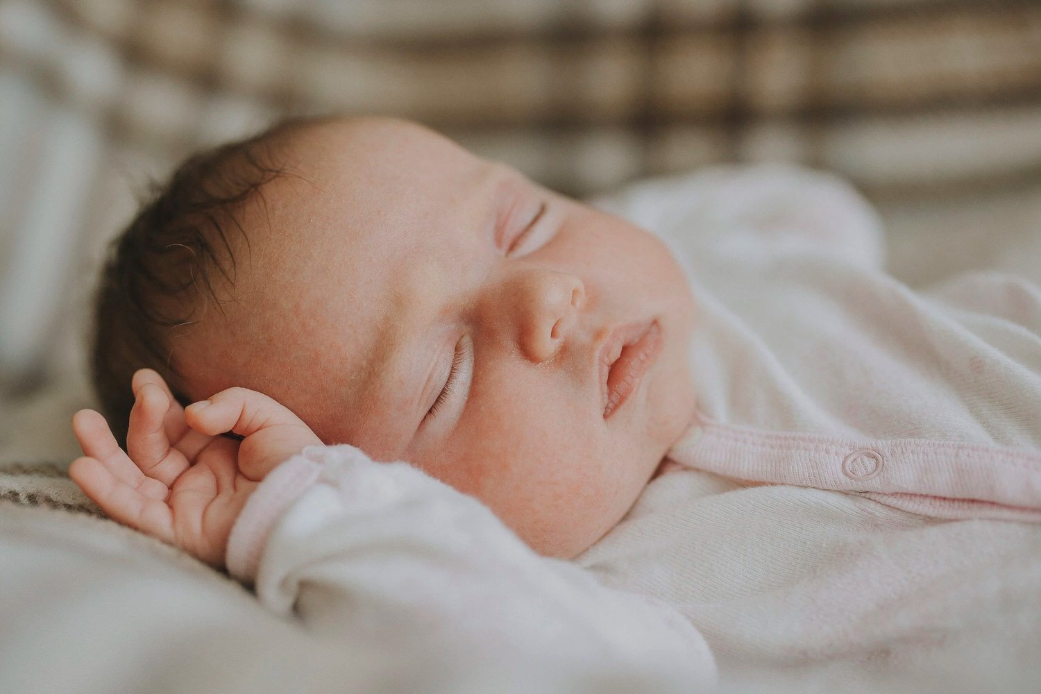 Close-up of a sleeping baby with a soft expression, lying on a blanket.