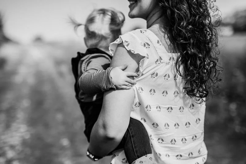 A woman holding a young child outdoors in black and white, with a blurred background.