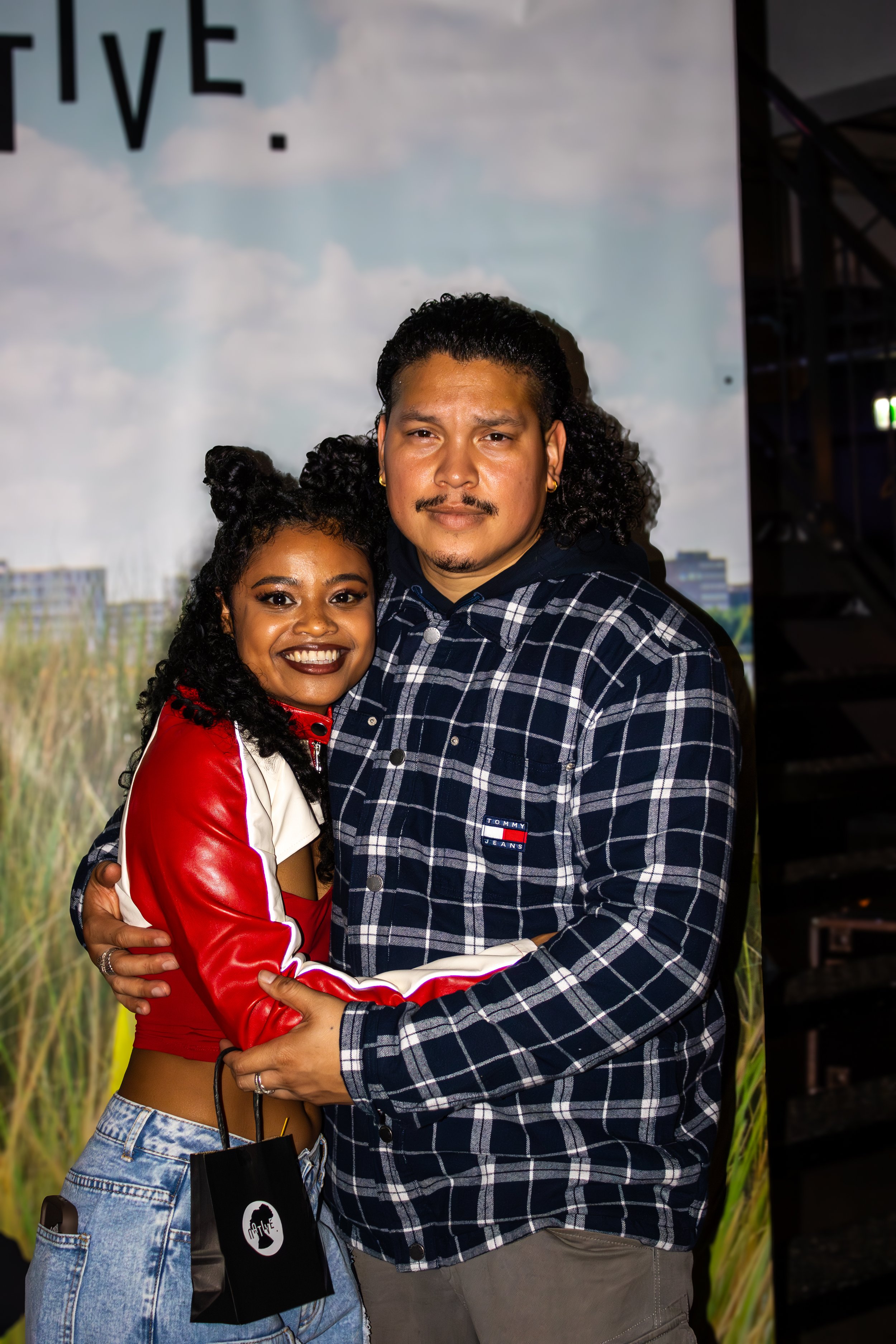 A woman and man hugging and smiling at the camera at an indoor event.