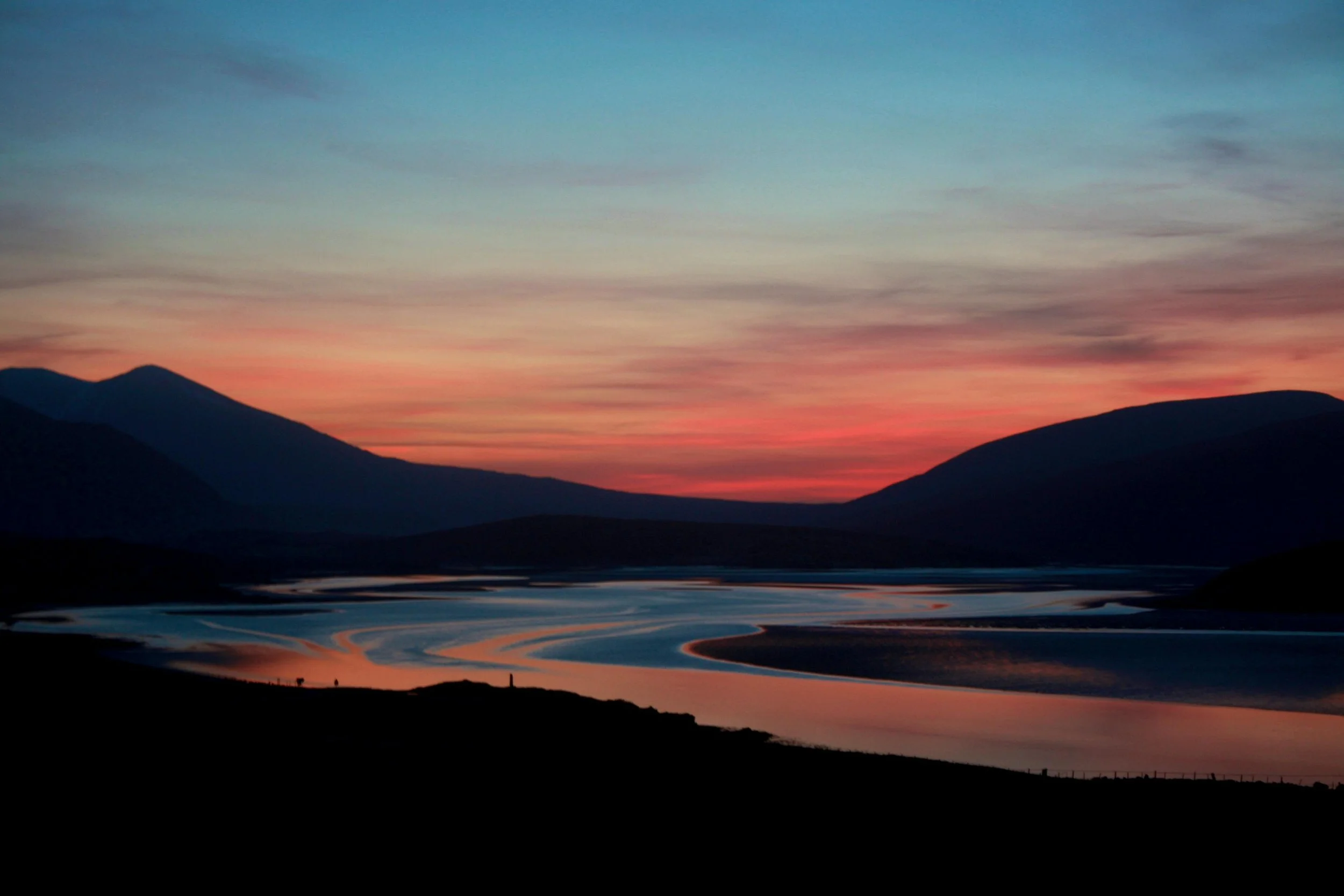 A scenic landscape at sunset with mountain silhouettes, a colorful sky, and winding rivers reflecting the sky's colors.