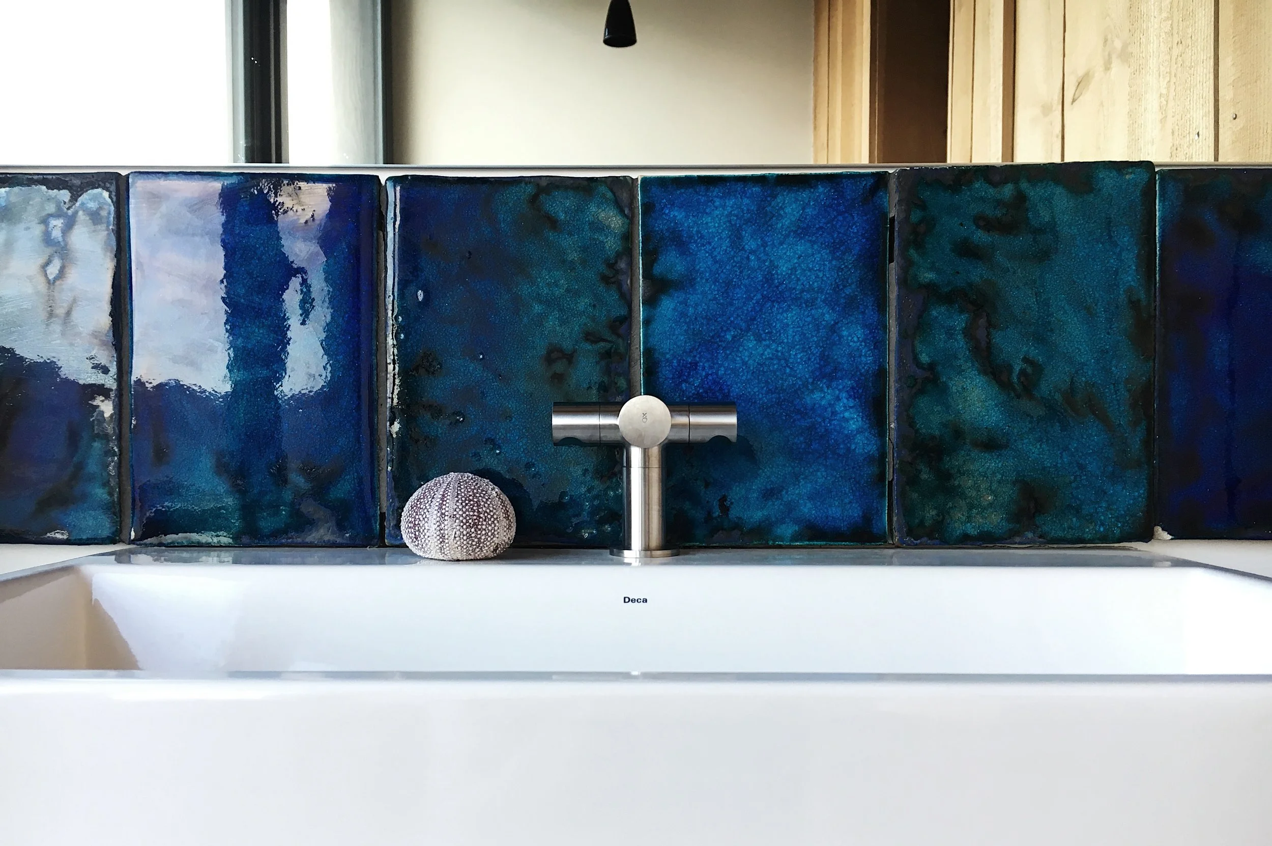 Close-up of a sink with blue and green patterned tile backsplash, silver faucet, and a small seashell decor piece on the left side.