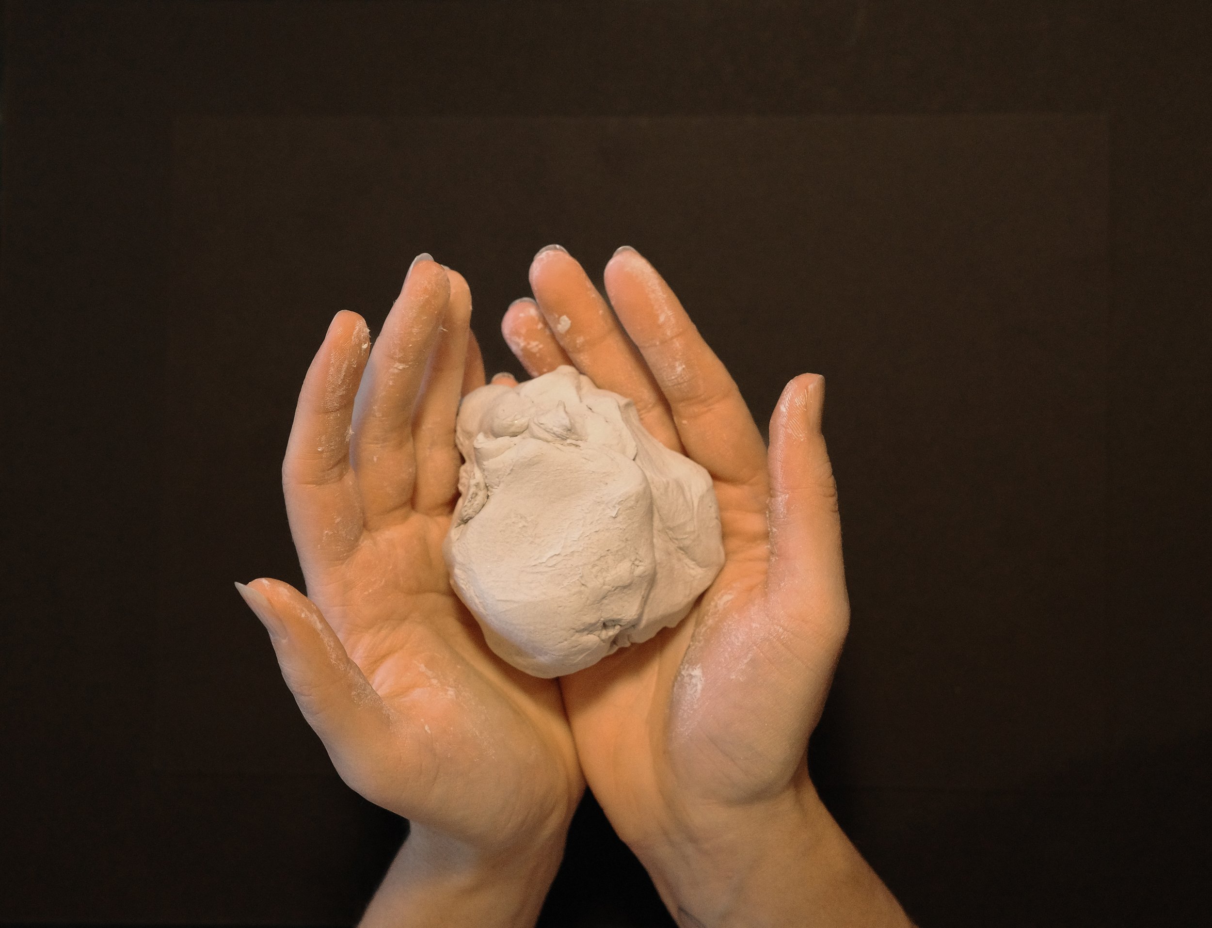 Two hands covered in flour holding a lump of dough.