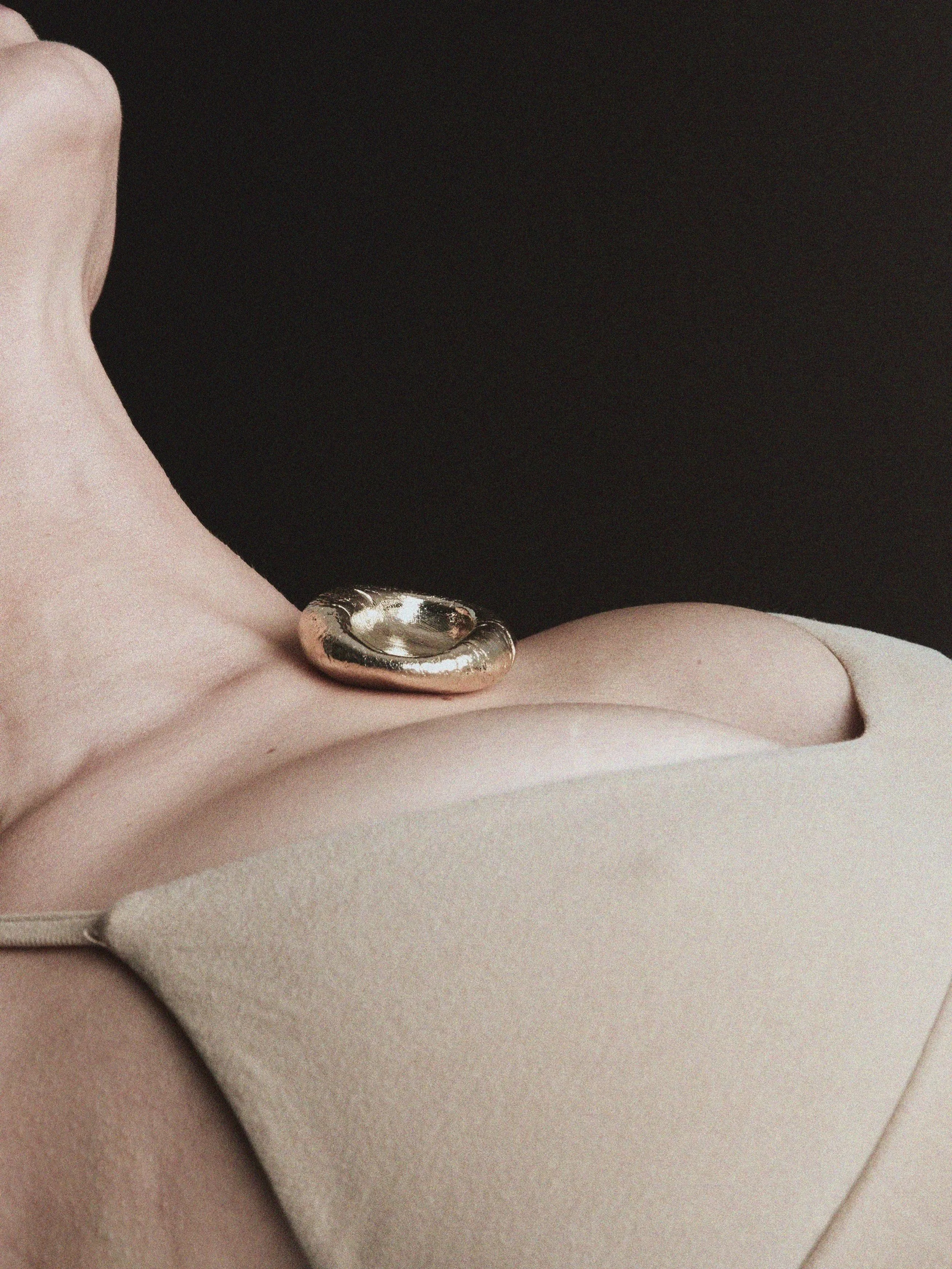 Close-up photograph of a person's shoulder and neck, wearing a beige top and a large, shiny, metallic metallic necklace.