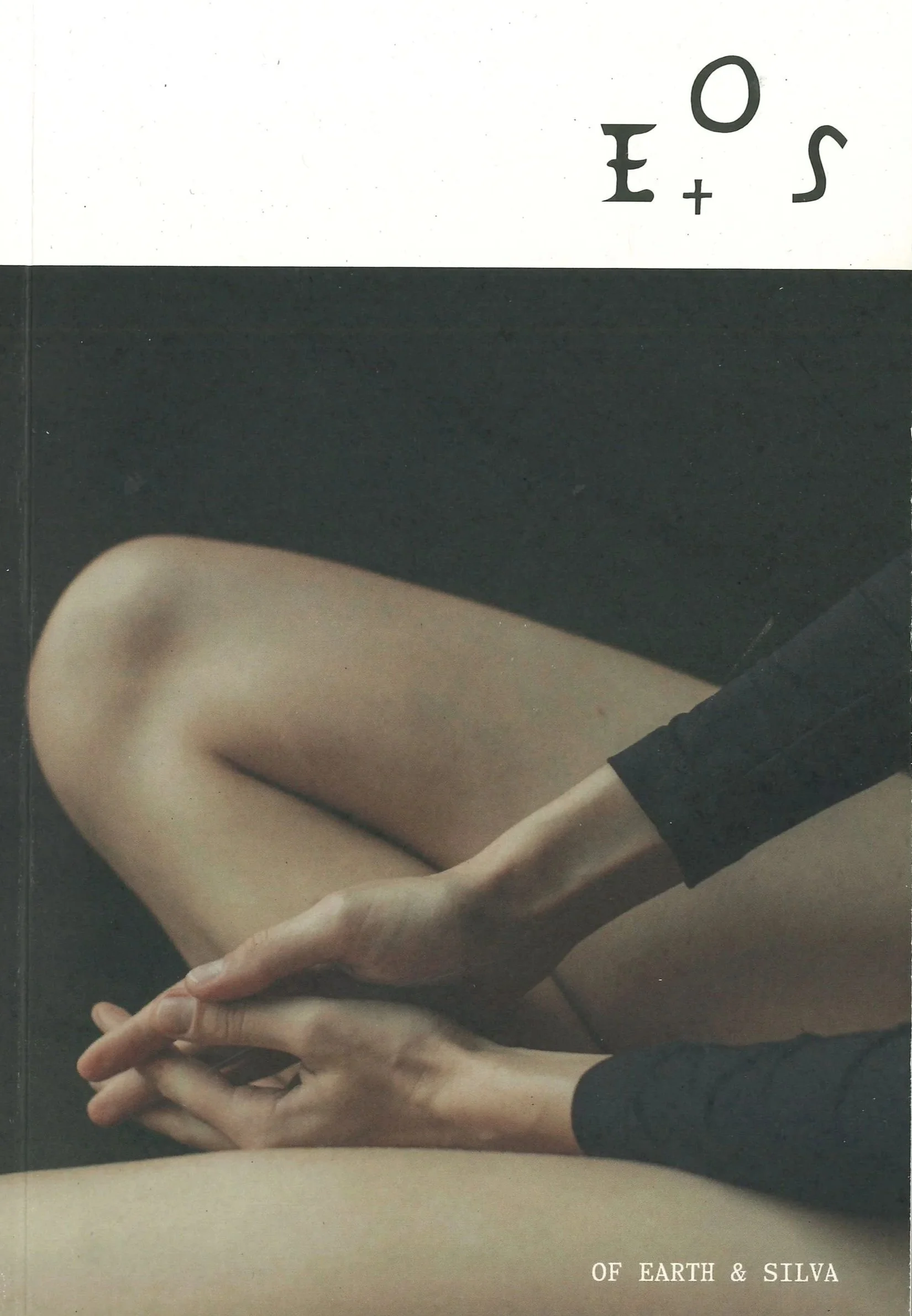 Close-up of a person's legs and hands, with one hand resting on the knee and the other hand clasped over it, wearing black clothing. The background is dark, and there is text that reads "OF EARTH & SILVA" at the bottom.