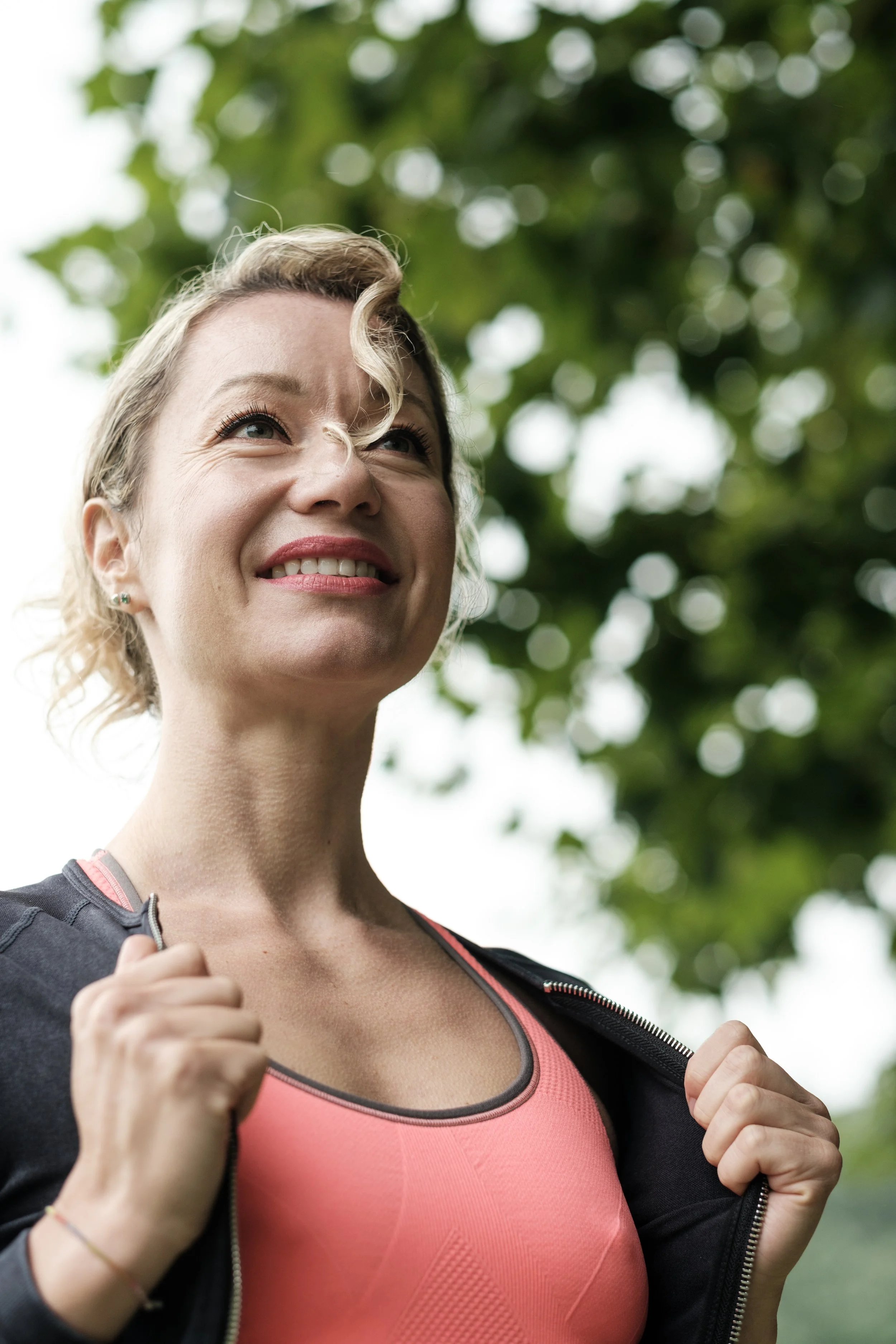 Mujer menopáusica con ropa deportiva y mochila, sonriendo, al aire libre con árboles en el fondo.