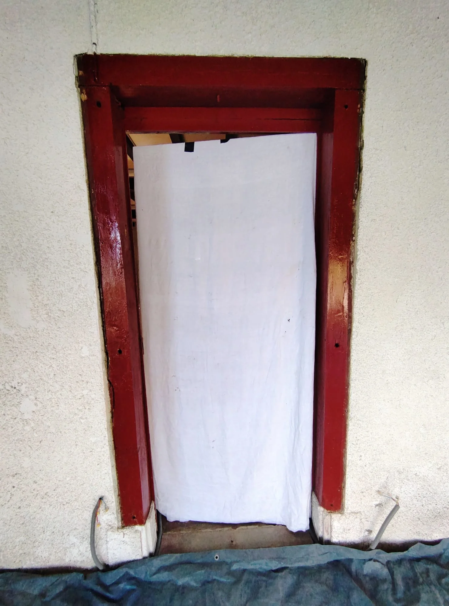 Une porte encadrée en bois rouge, couverte d'une draperie blanche, dans un mur en plâtre beige