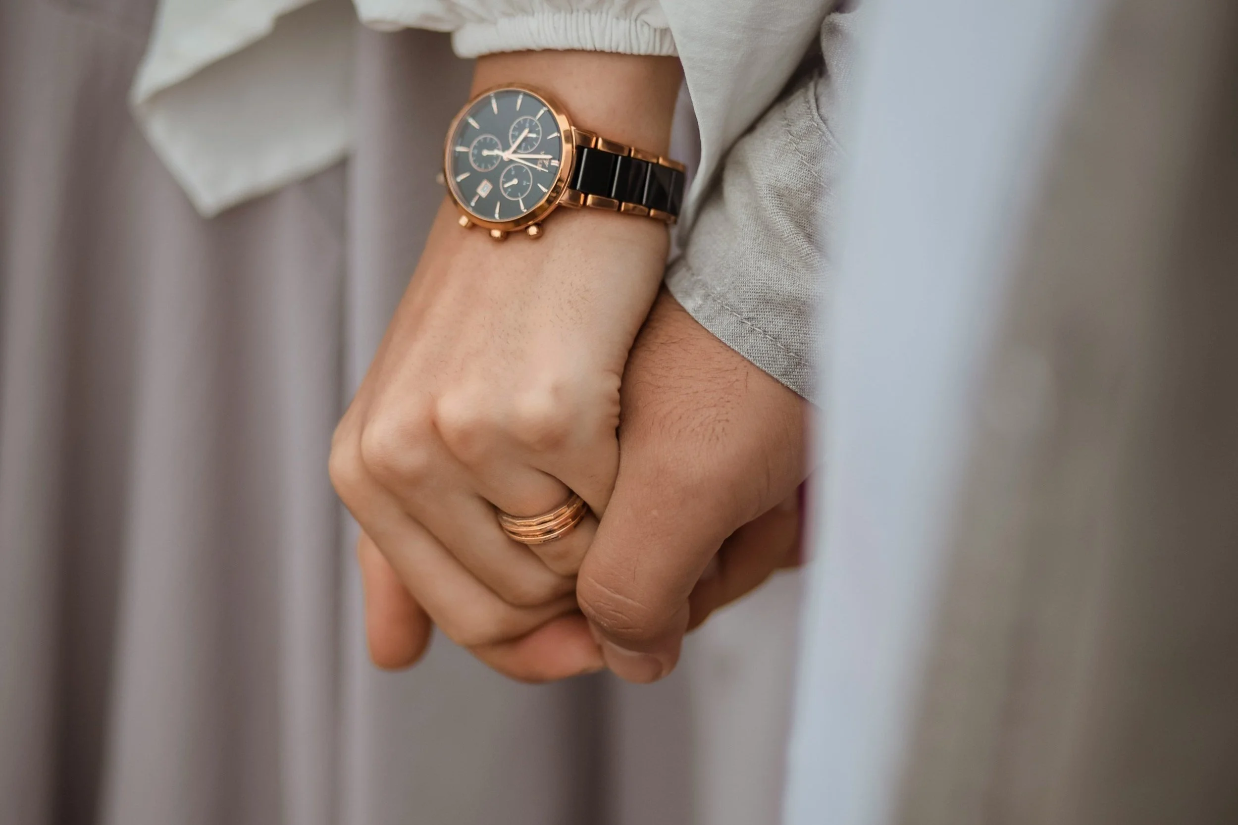 Close-up of two people holding hands, one wearing a wristwatch and a ring.