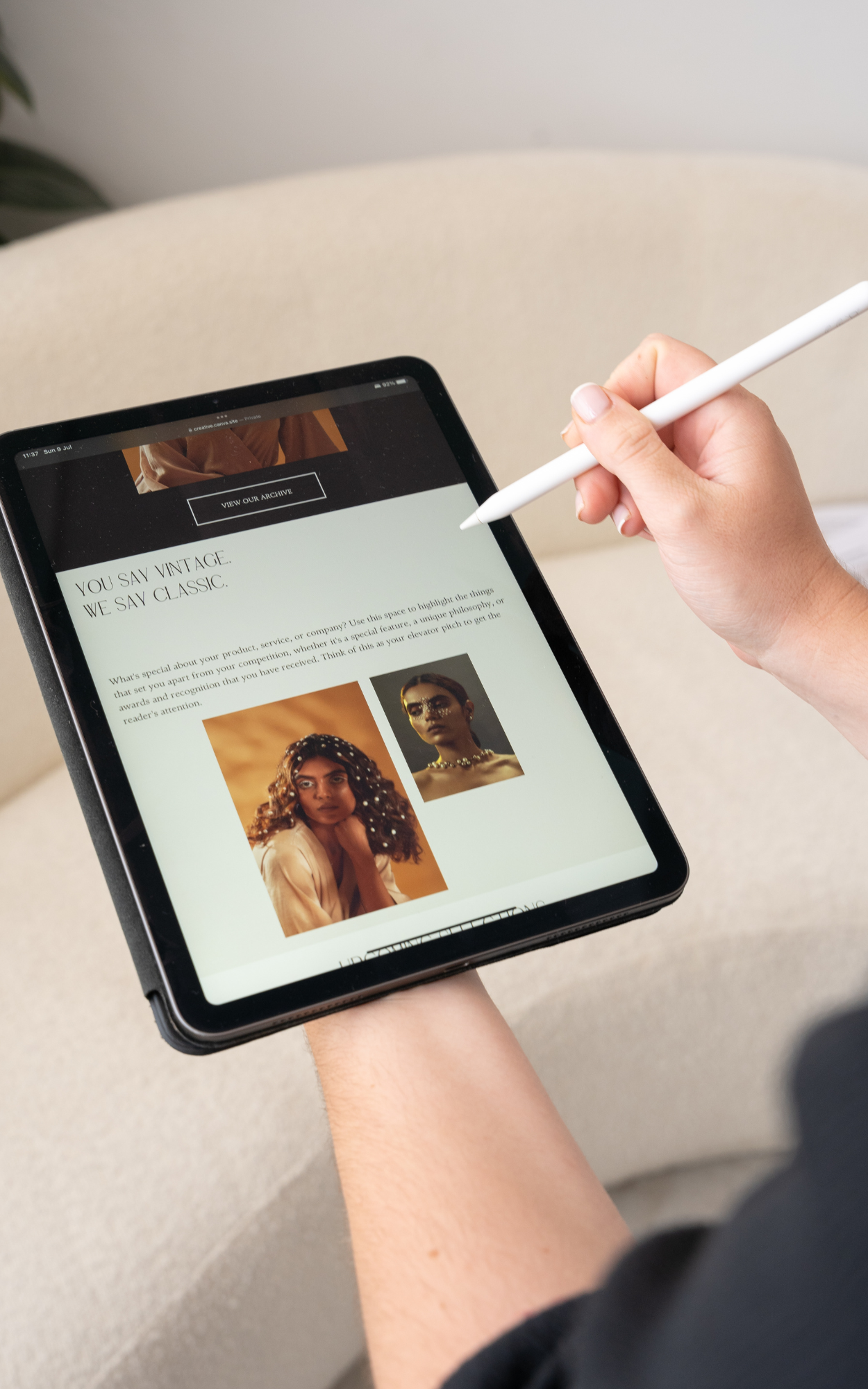 Person holding a tablet with a stylus, displaying a webpage featuring two women with curly hair and jewelry, and text about vintage and classic styles.