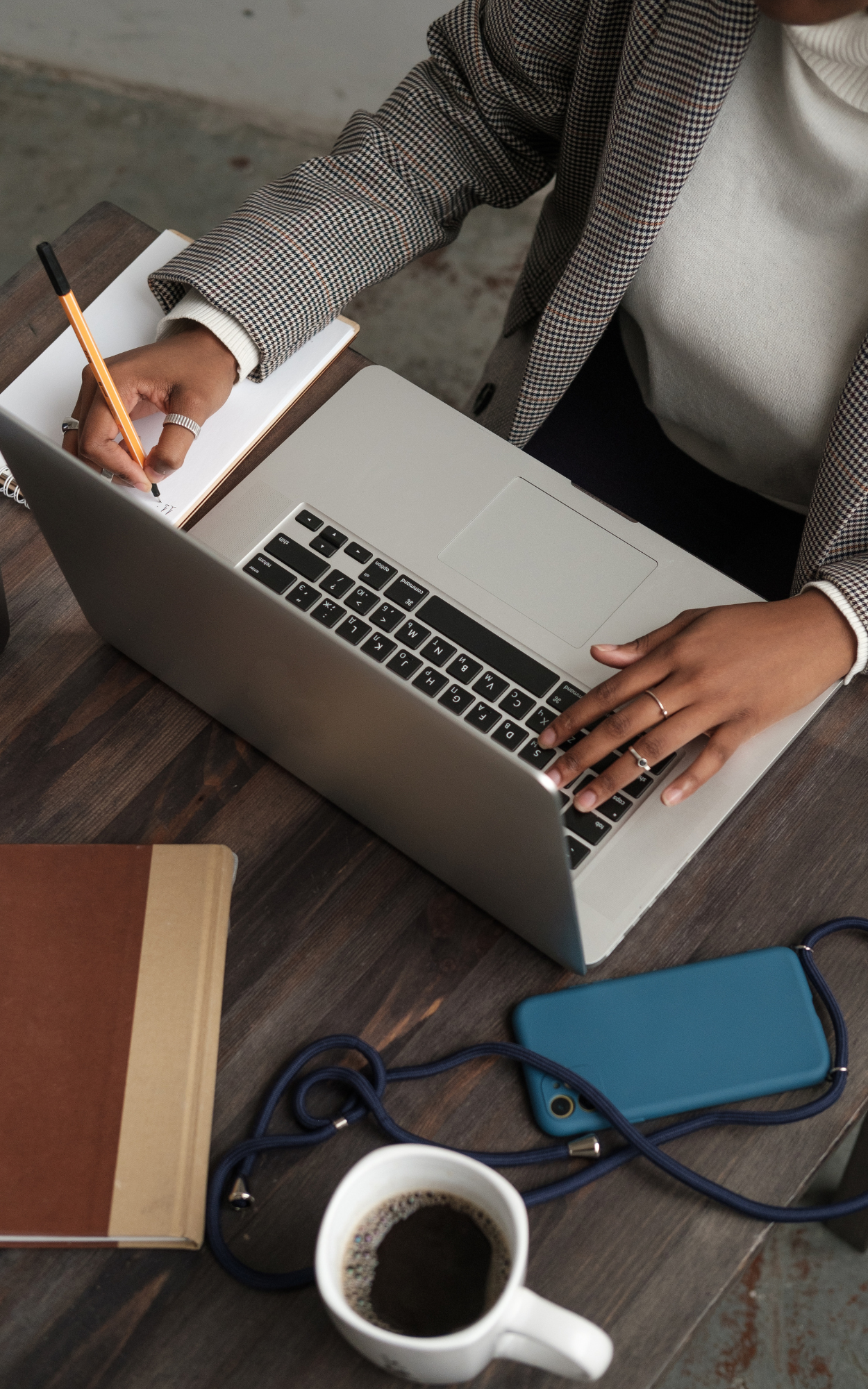 A person working at a desk with a laptop, notepad, smartphone, and a cup of coffee.