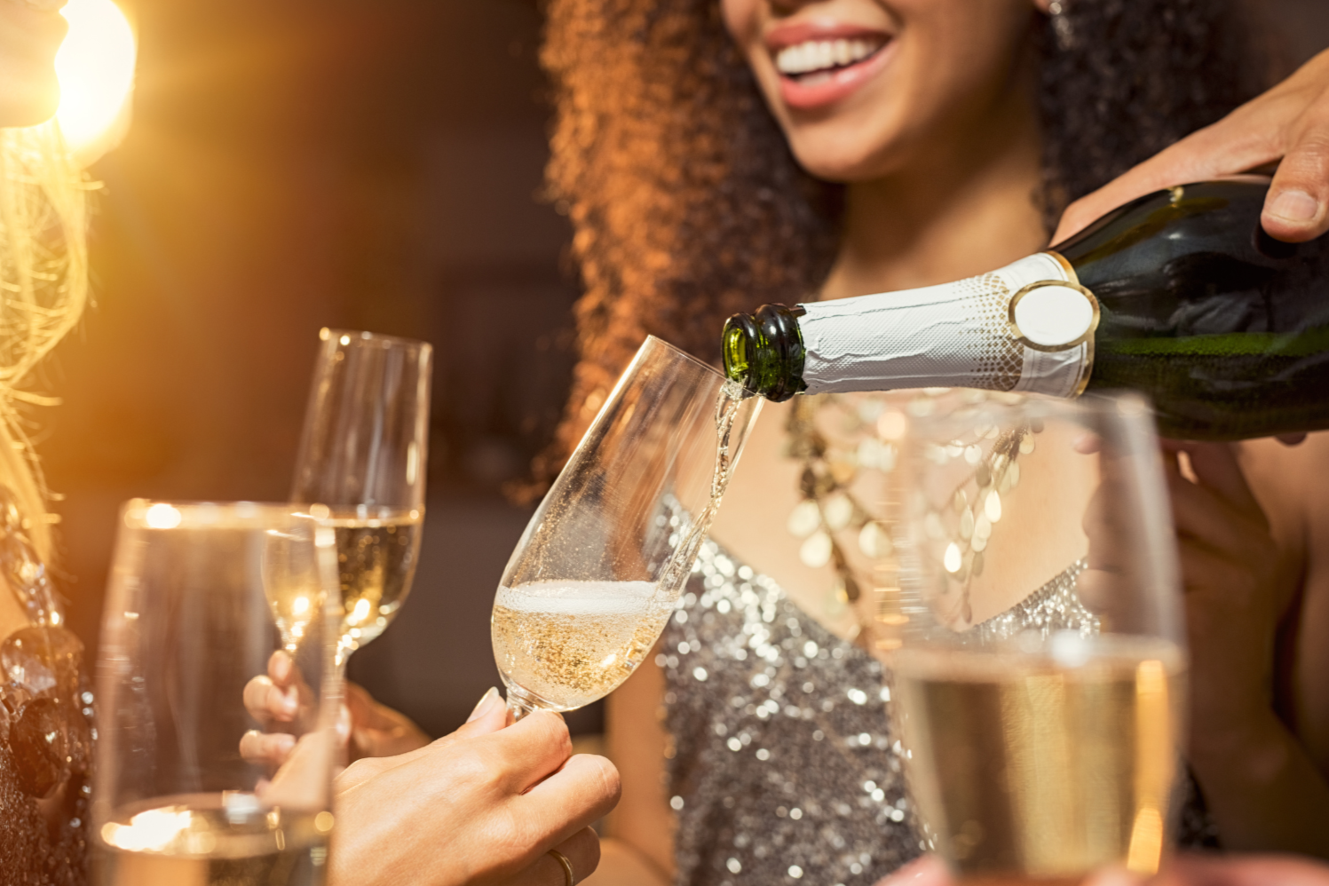 Woman with curly hair and a shiny dress pours champagne into a flute at a celebration party.