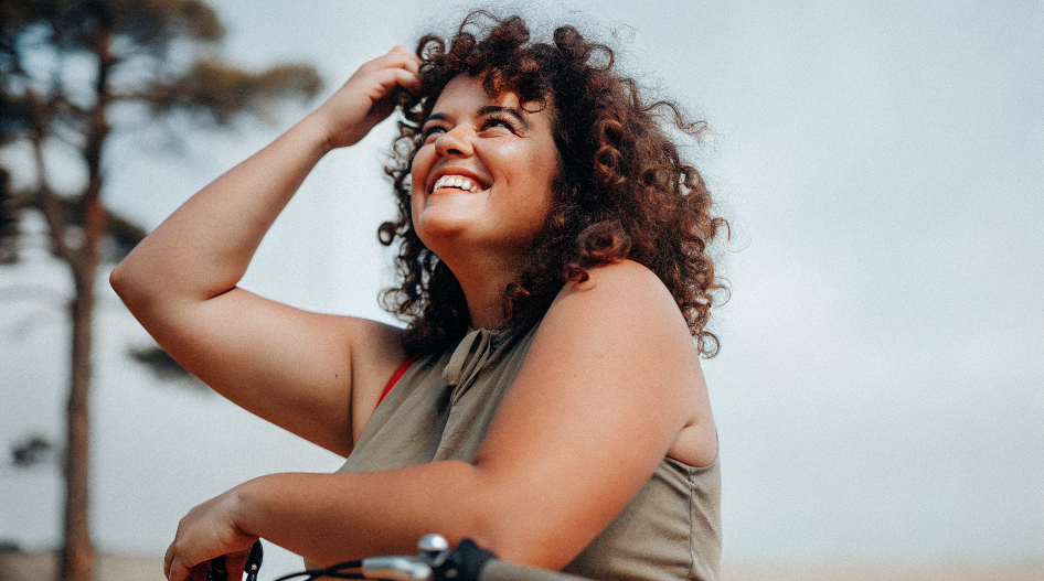 Hymyilevä nainen luonnon keskellä, taustalla puita ja taivasta.