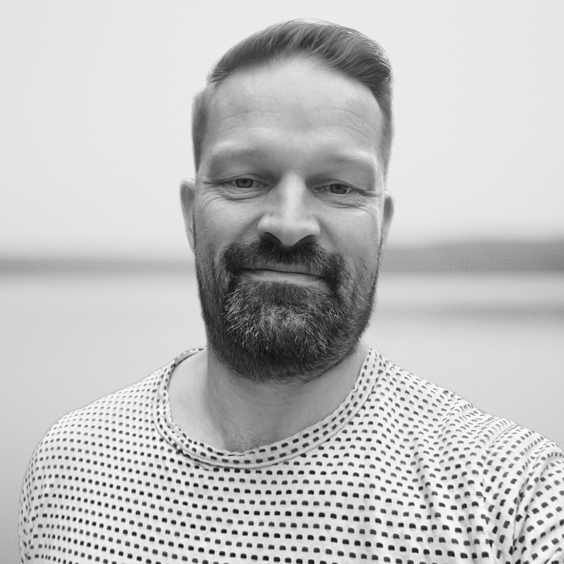 Mies poseeraa kameralle mustavalkoisessa kuvassa, paita jossa pieni kuviokuvio.