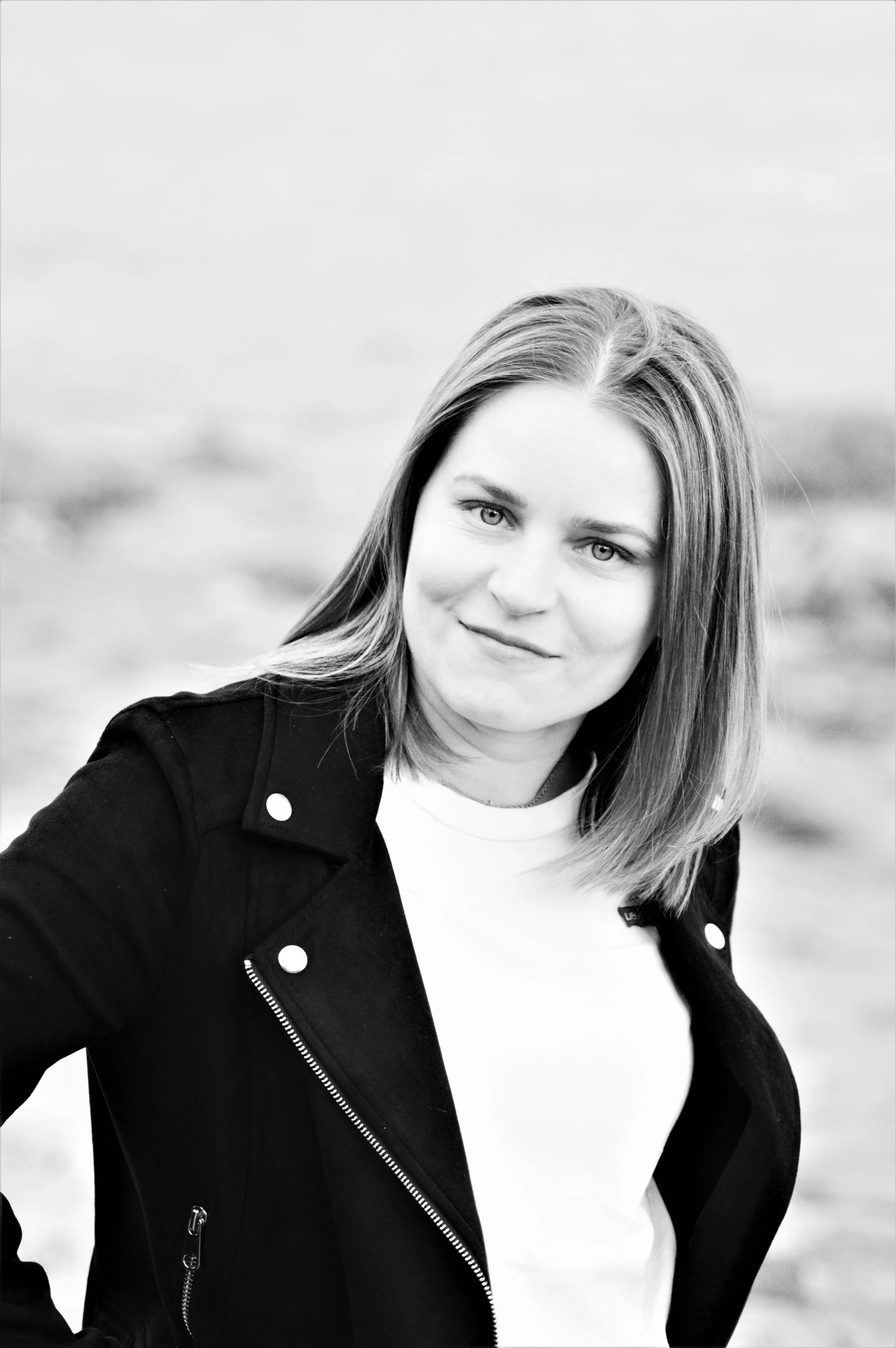 Mustavalkokuva nuoresta naisesta, jolla on vaaleat hiukset, pukeutuneena mustaan takkiin ja valkoiseen t-paitaan, taustalla epämääräinen maisema.