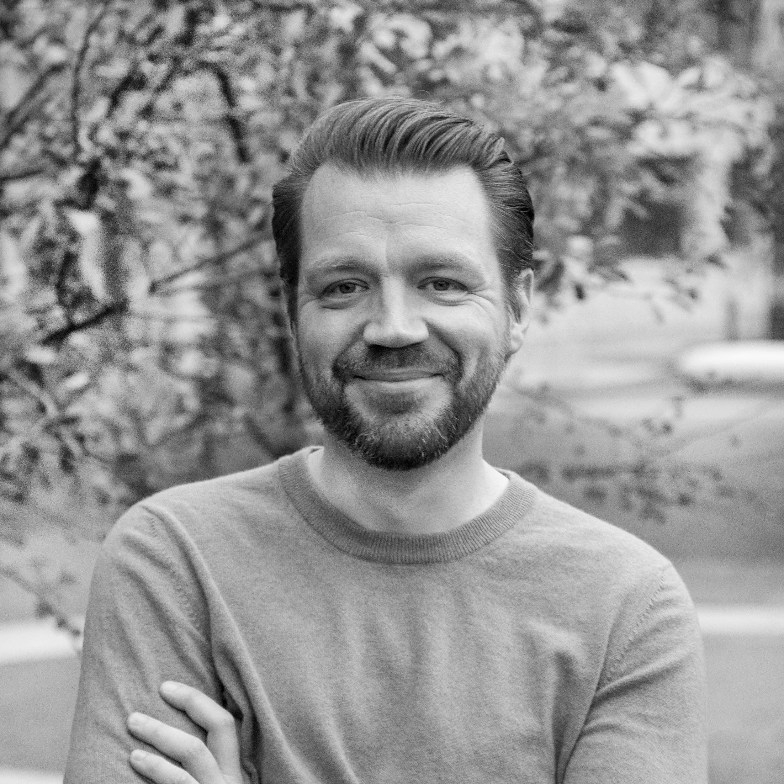 Mies hymyilee ulkona, taustalla puut ja puuraja.