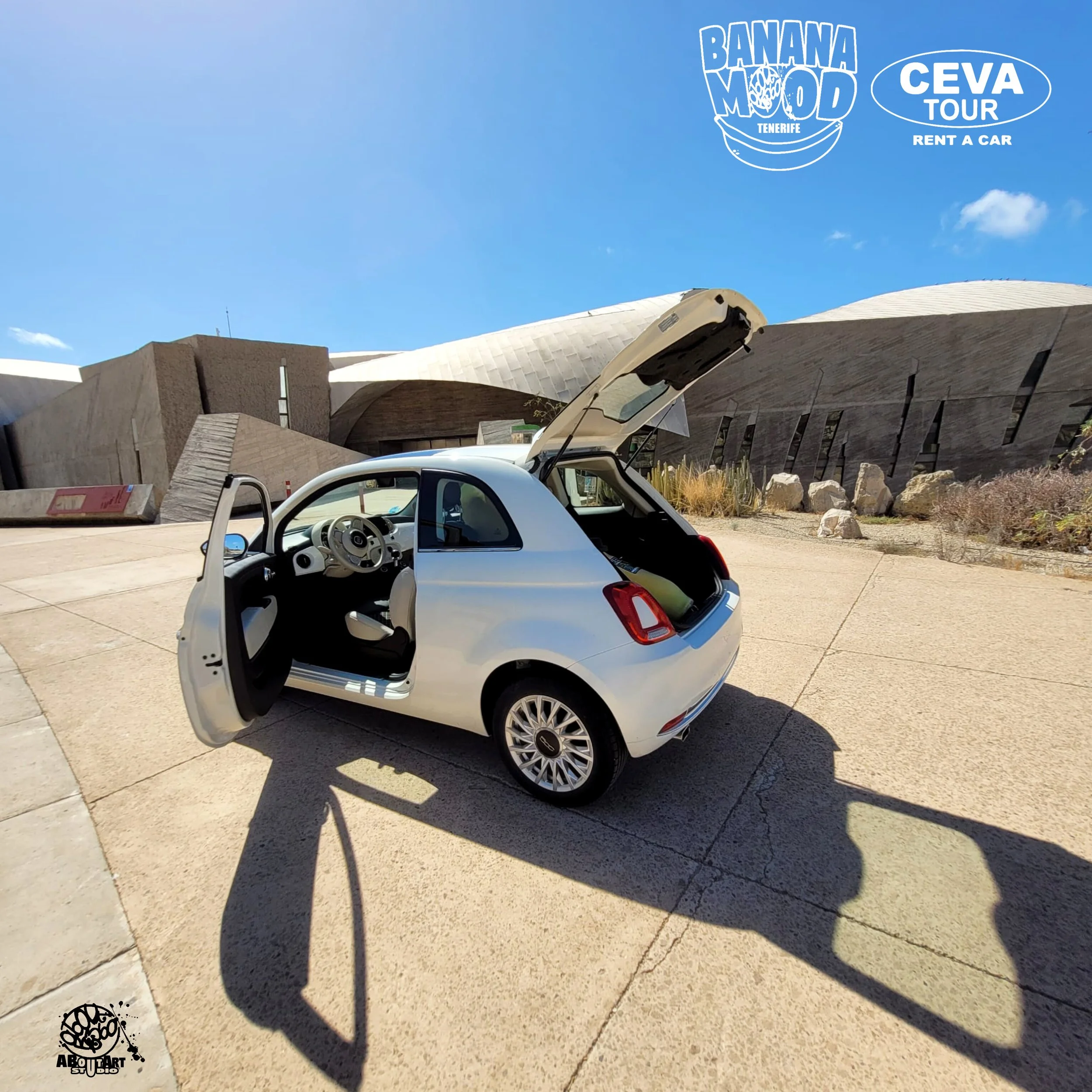 Coche de juguete blanco con las puertas abiertas y maletero, en un área exterior con edificios modernos y un cielo despejado, en el Museo de la Ciencia y el Cosmos en Tenerife.