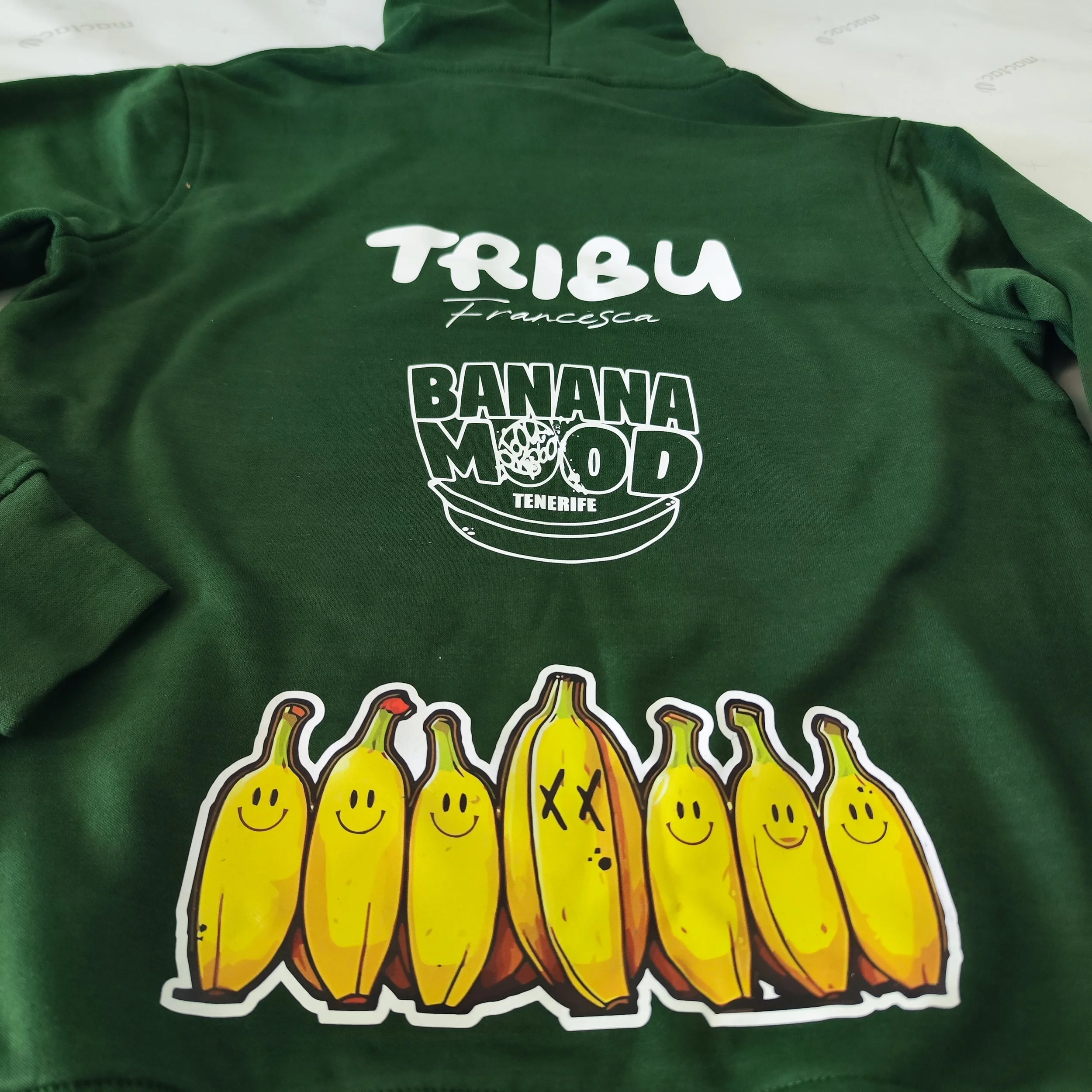 Camiseta verde con logotipos y dibujos de bananas y texto en español.